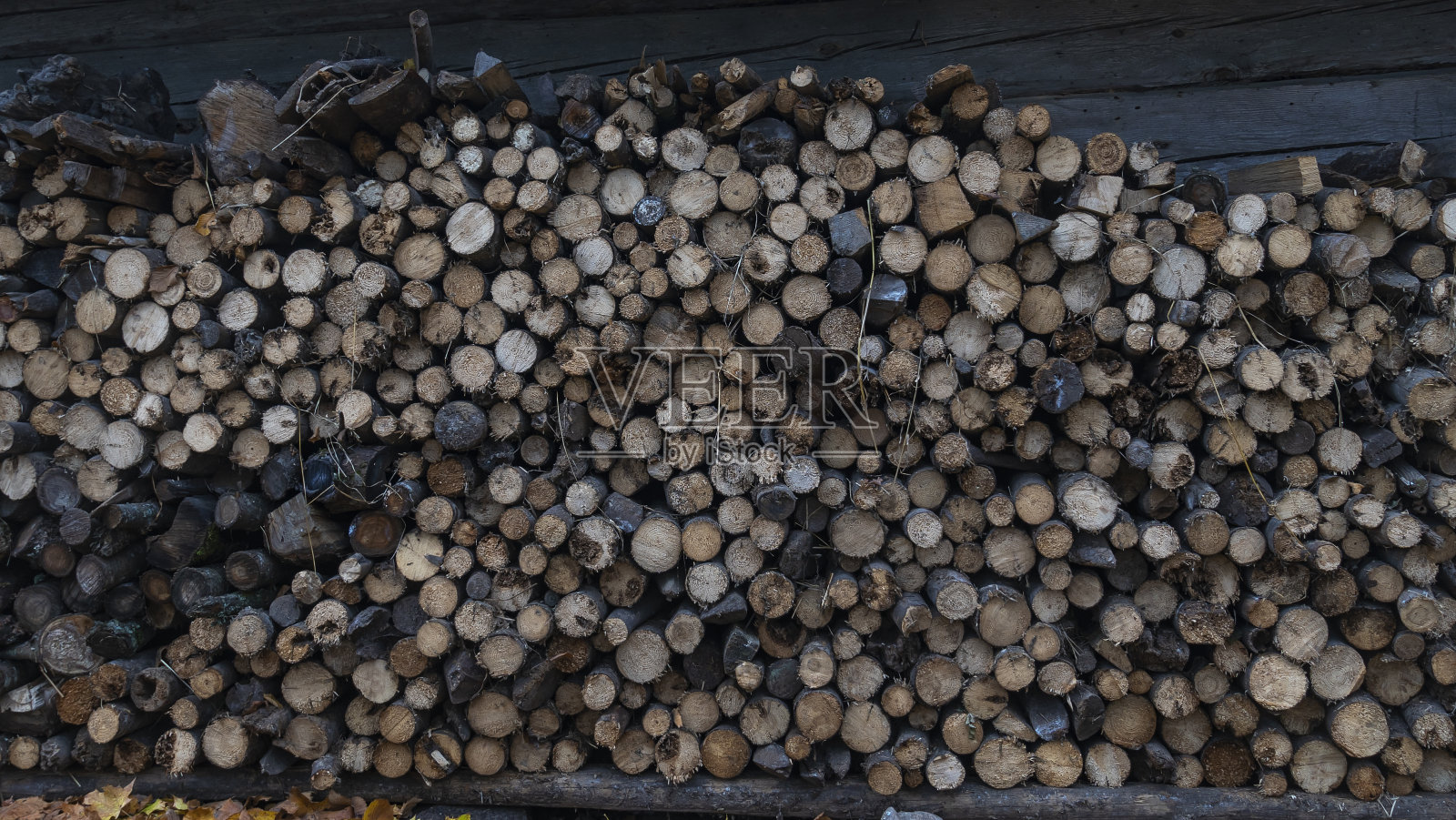 在老式木谷仓的墙上整齐地堆放着一大堆为冬天准备的砍好的柴火。结构设计。照片摄影图片