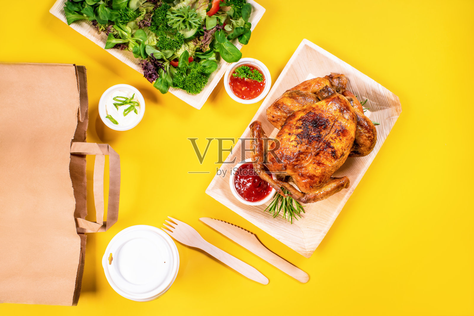 整个烤鸡。纸盒烤鸡。烤鸡和蔬菜放在硬纸板盘子里带走，容器底色为黄色。照片摄影图片