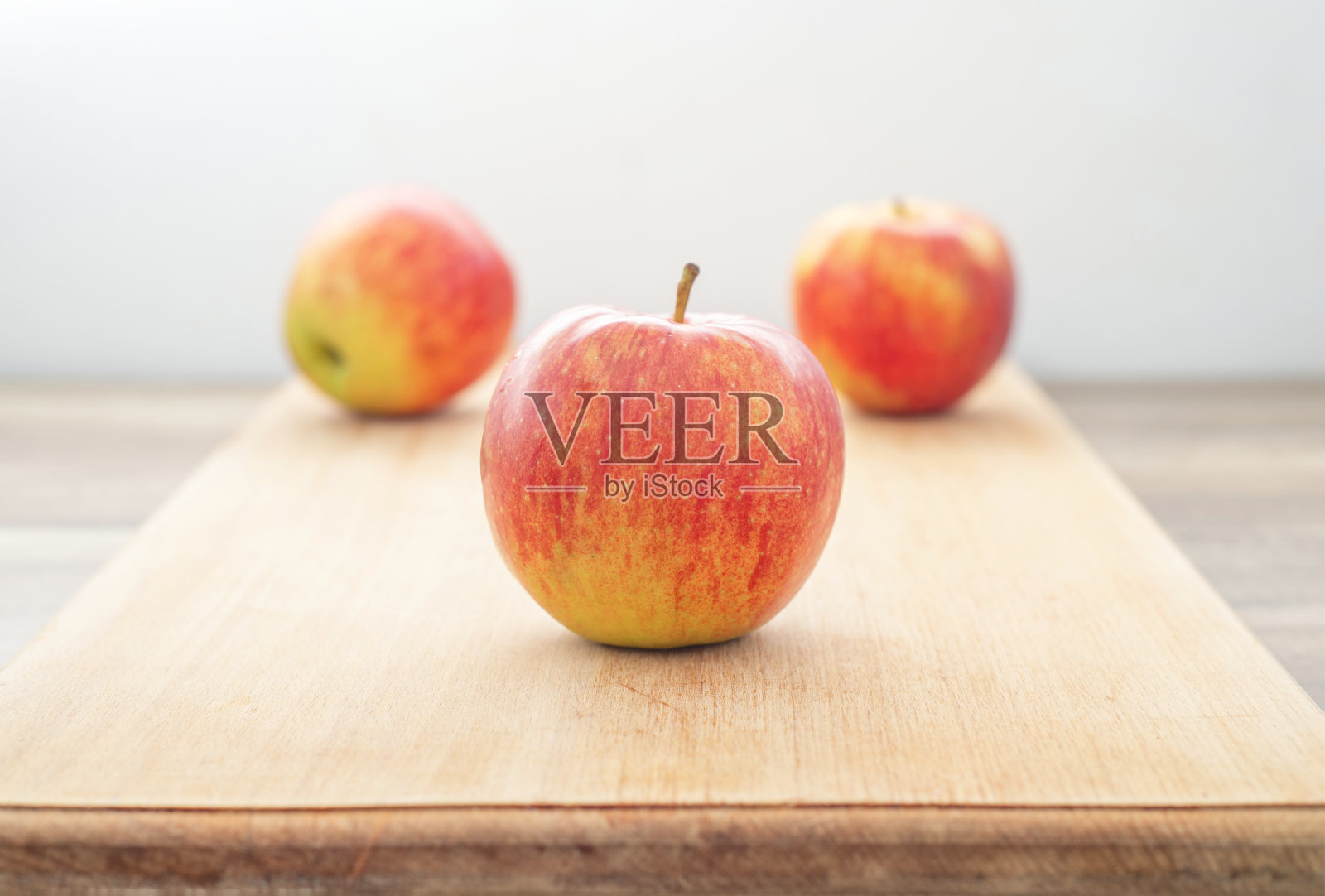 灰色背景上，木桌上放着红色多汁的苹果。照片摄影图片