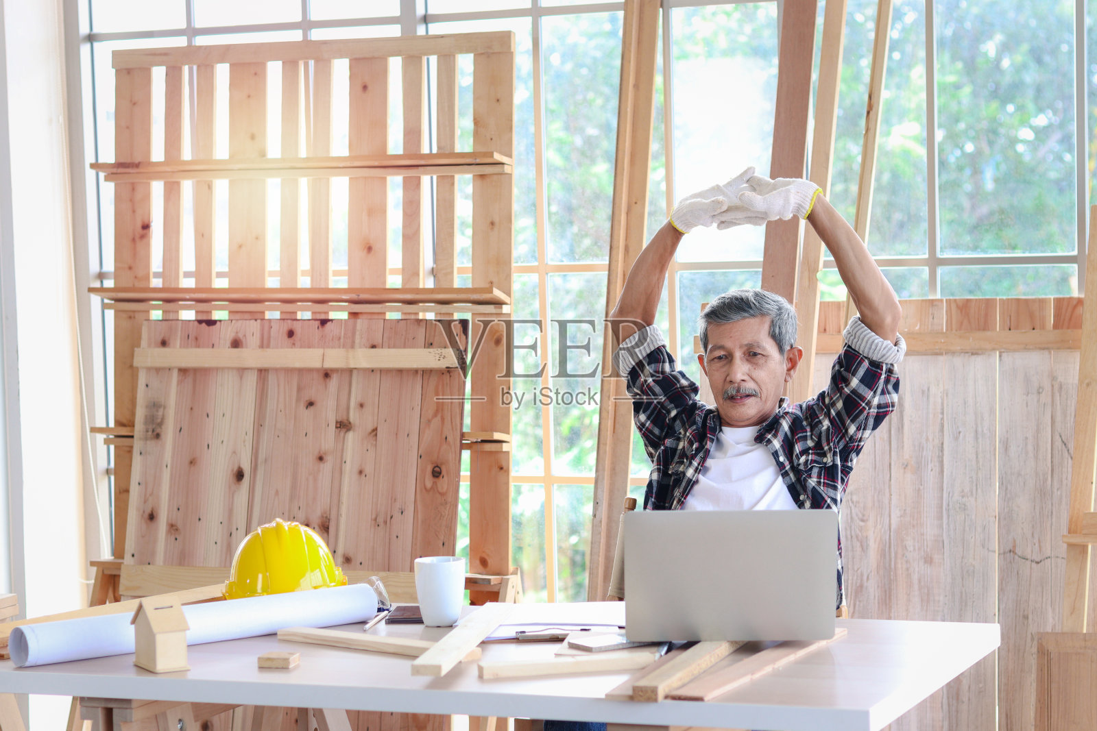 上了年纪的亚洲木匠在木工车间的办公桌上休息，喝着咖啡照片摄影图片