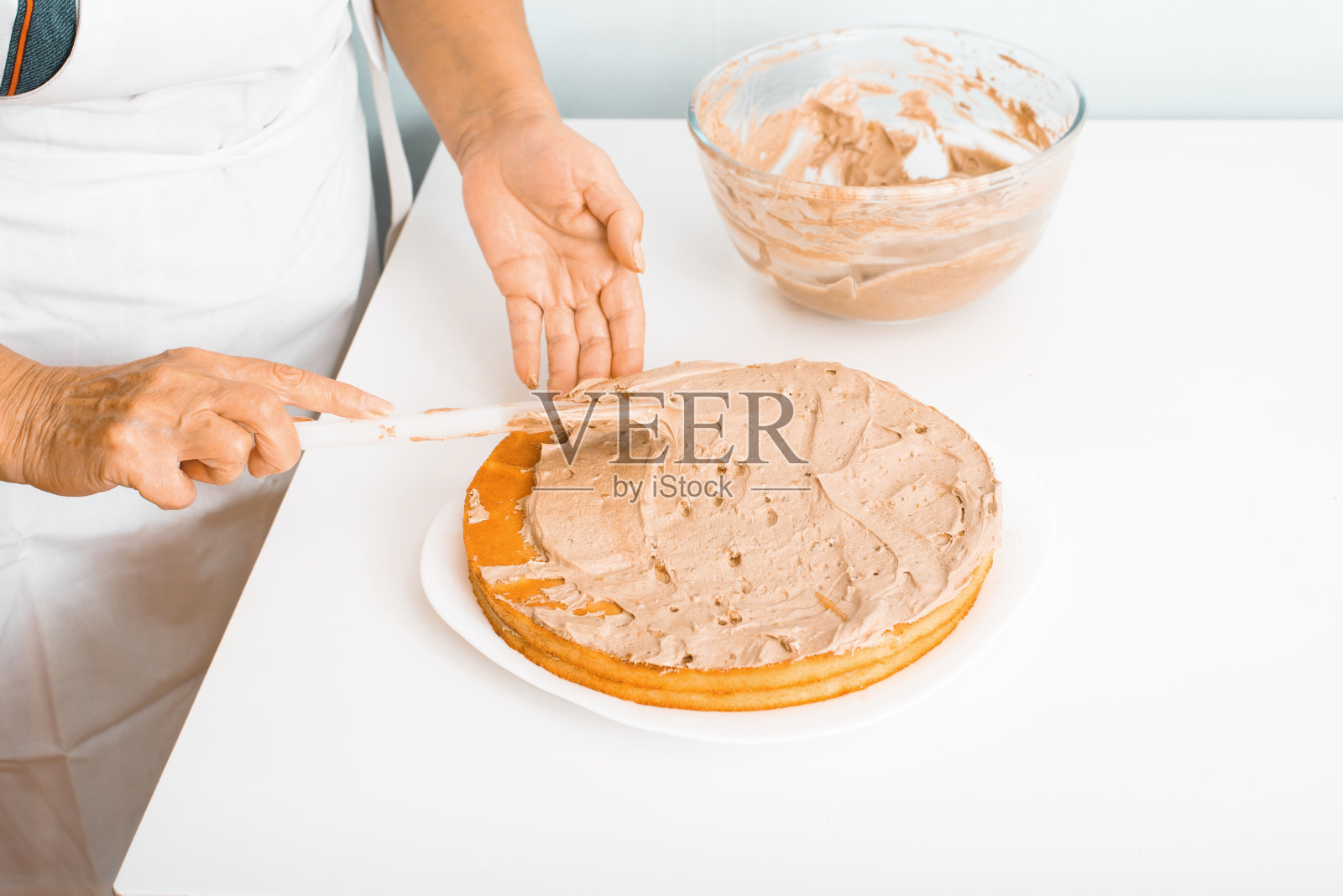 妇女用刮刀烹饪奶油馅蛋糕，家庭主妇在室内厨房准备美味的分层蛋糕，特写镜头。美食爱好的概念照片摄影图片