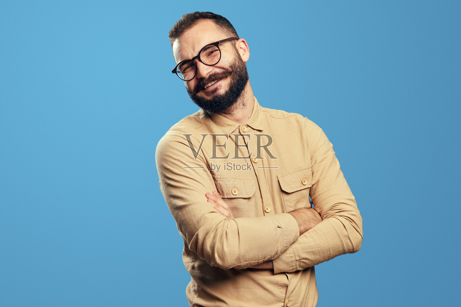 年轻英俊的男子交叉双手微笑，看着蓝色的相机照片摄影图片