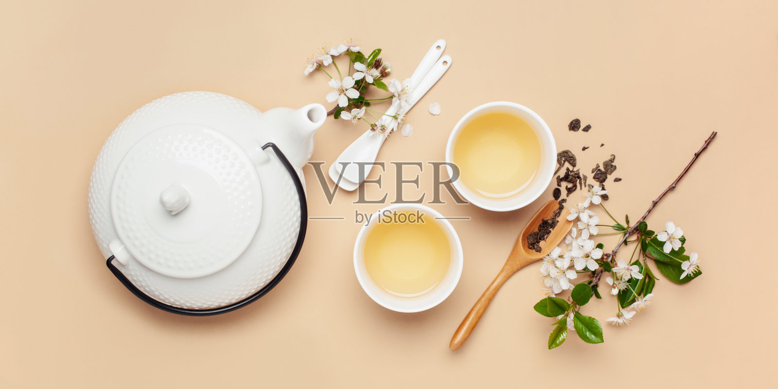 春天的茶道。花草茶在杯子，茶壶和开花的樱桃枝。前视图。平躺照片摄影图片