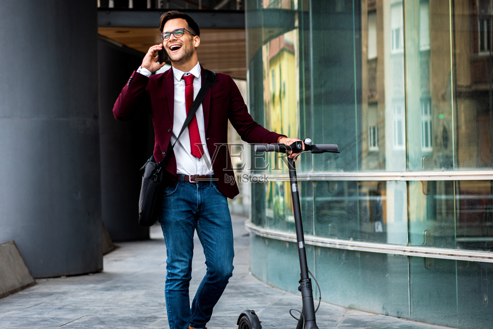 微笑的商人骑着电动车站在现代商业大厦前。照片摄影图片