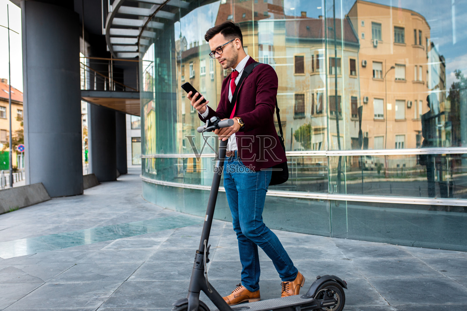 微笑的商人骑着电动车站在现代商业大厦前。照片摄影图片
