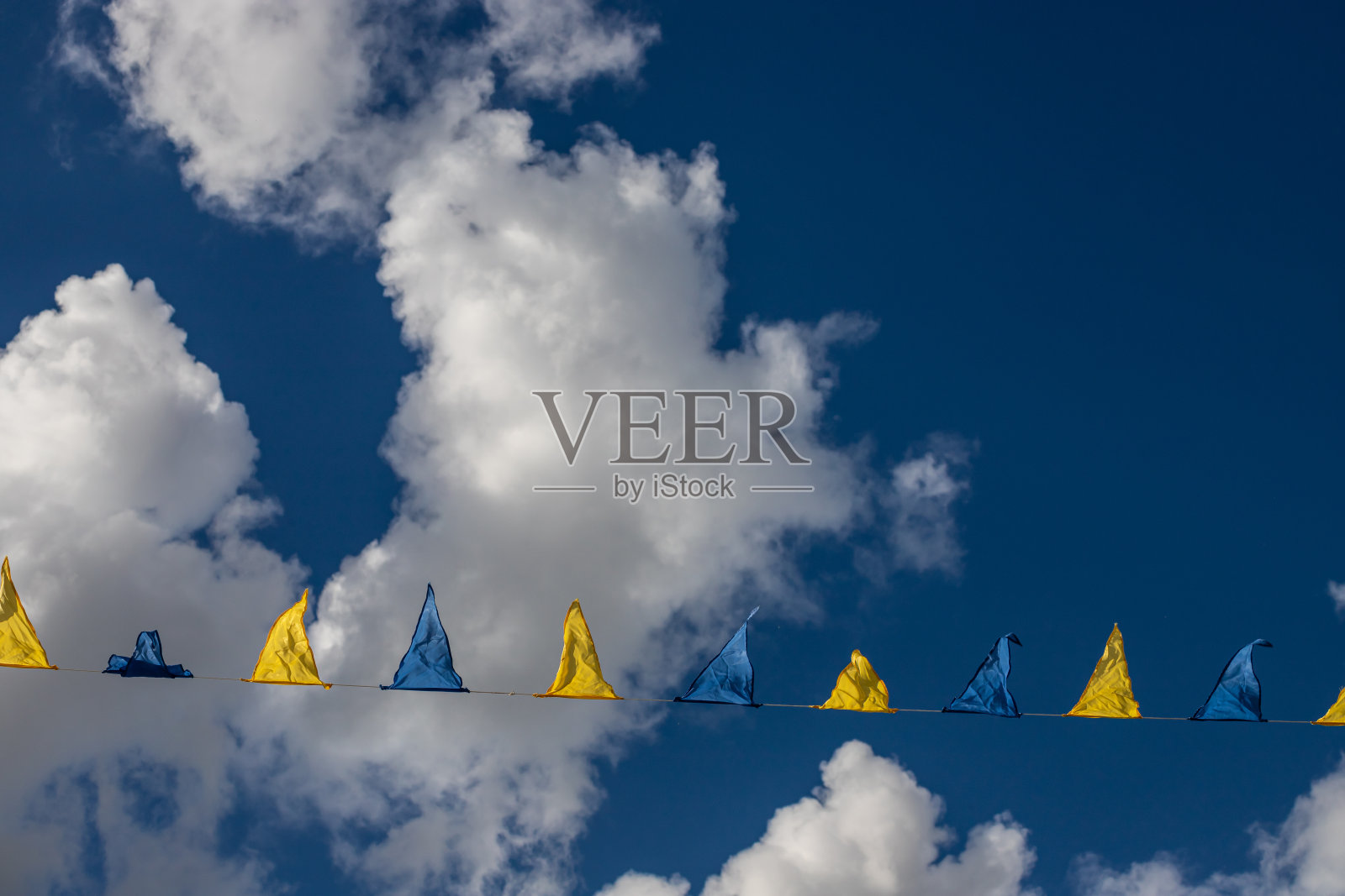 黄色和蓝色三角形的节日旗帜在天空背景与白云。户外庆祝聚会照片摄影图片