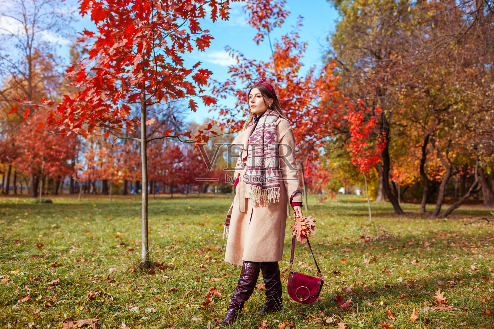 全身画像的美丽的女人穿着时尚的衣服，靴子，配件在秋天公园。女性秋季时尚照片摄影图片