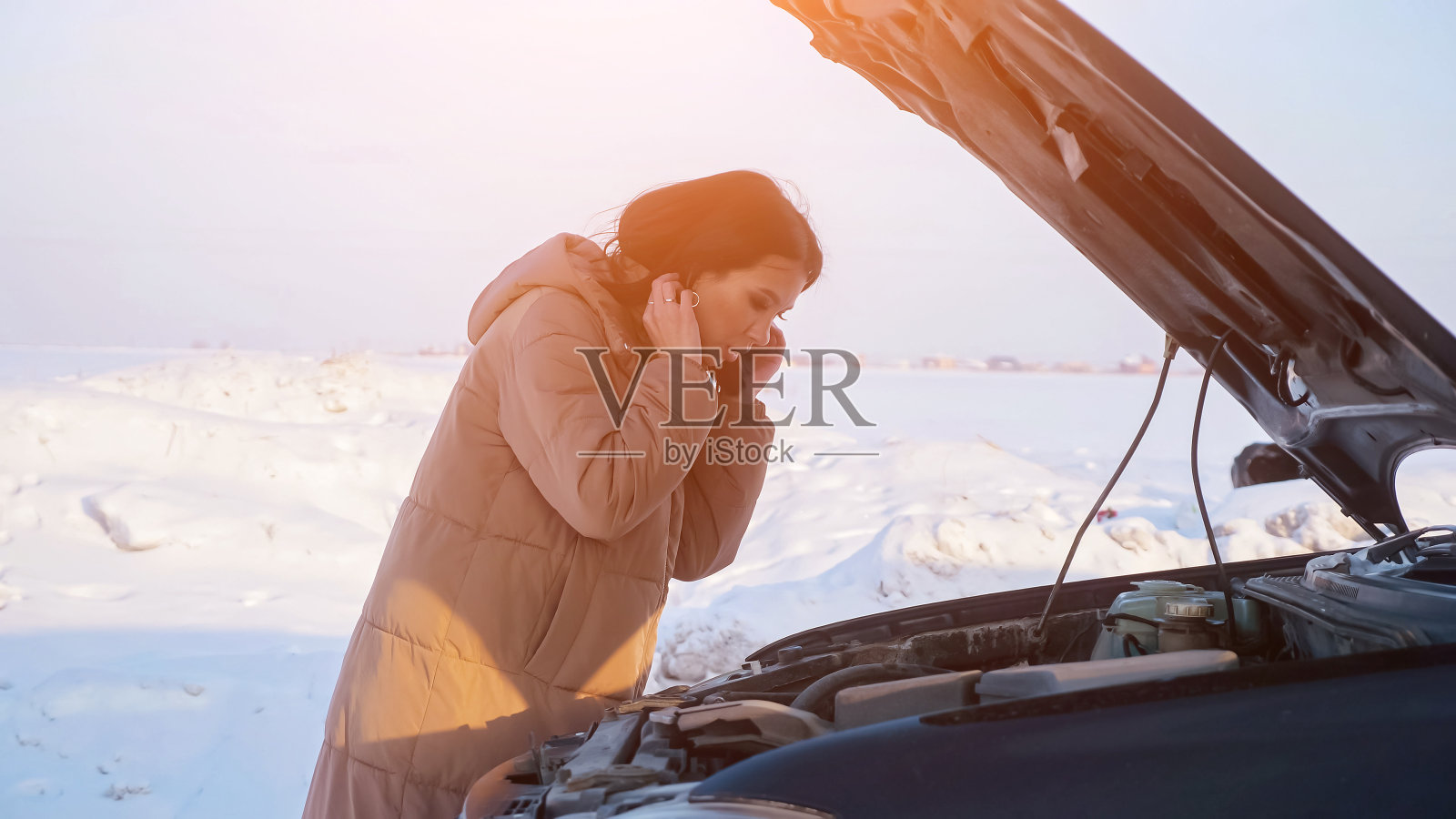 在下雪的路上，一个沮丧的女人看着坏掉的汽车引擎照片摄影图片