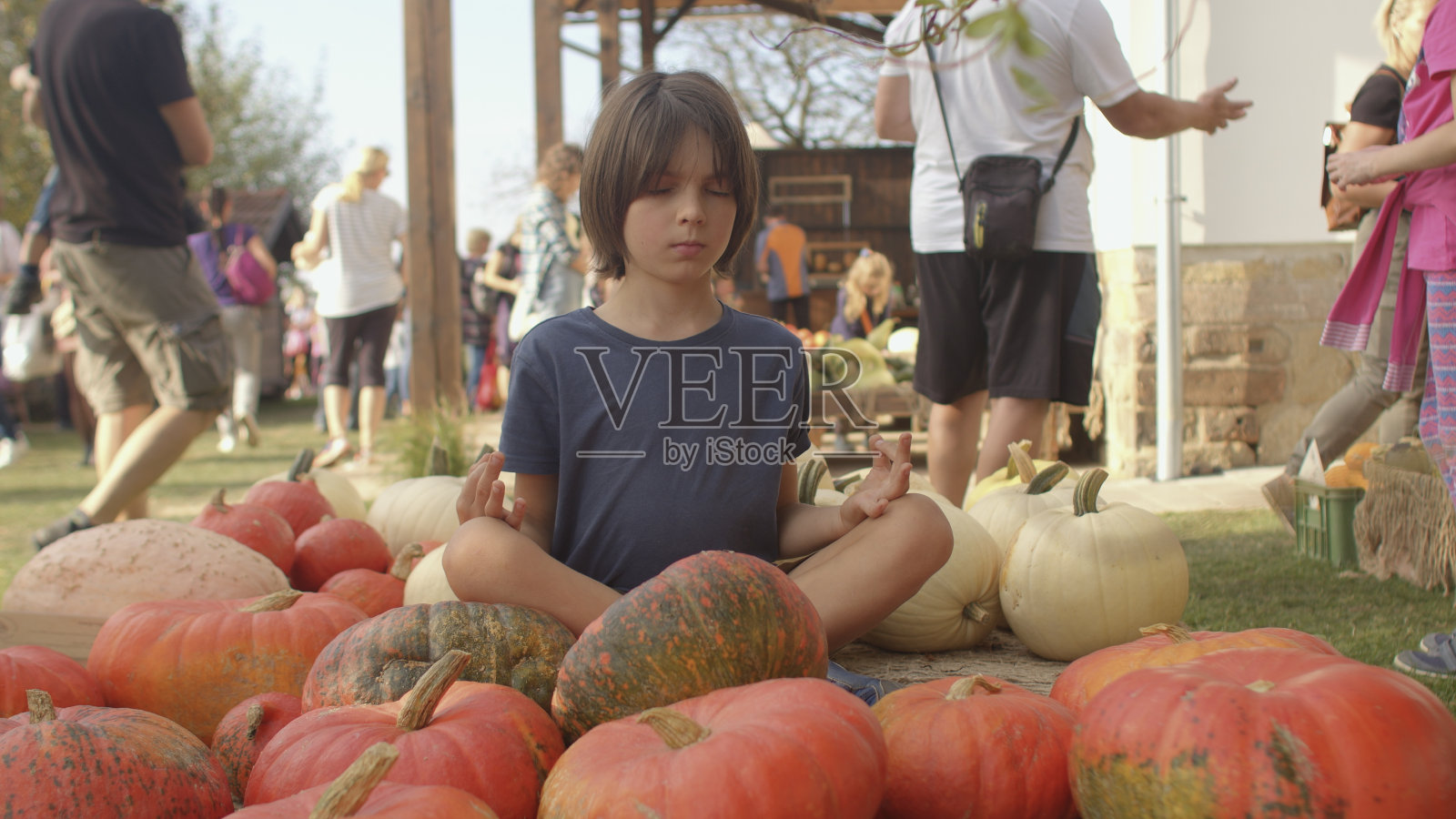 孩子以莲花姿势冥想，坐在橙色南瓜，农贸市场。照片摄影图片