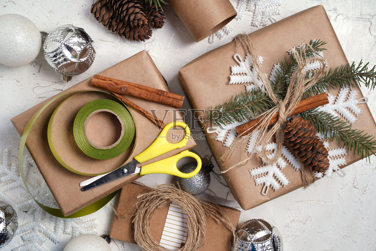 用麻绳带用牛皮纸包装圣诞节日手工礼物。在圣诞礼品盒前鞠躬，白色的桌子上装饰着雪花，俯视图。照片摄影图片