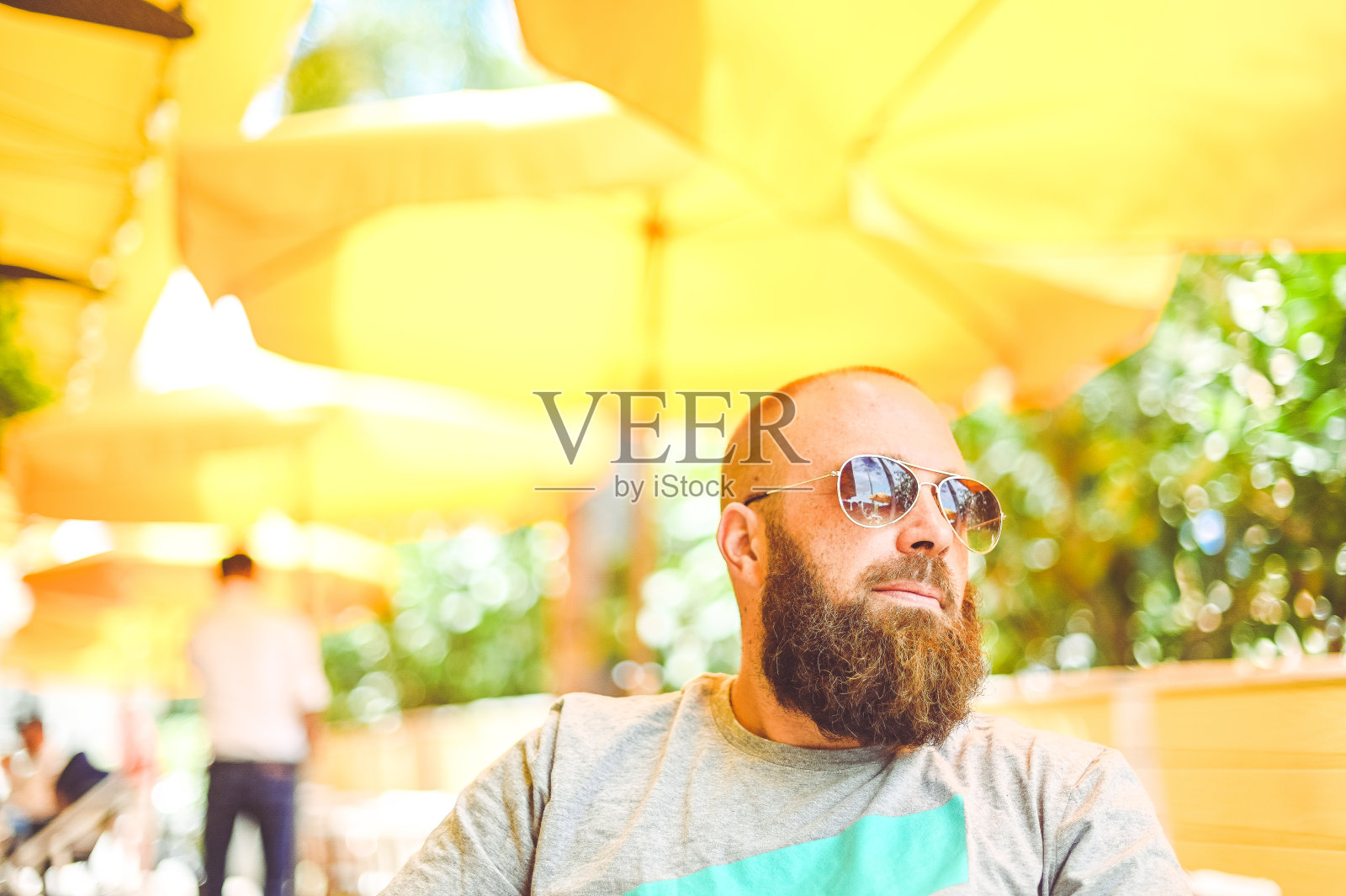 一名戴着太阳镜的男子在阳光明媚的黄色户外咖啡馆或餐厅休息照片摄影图片