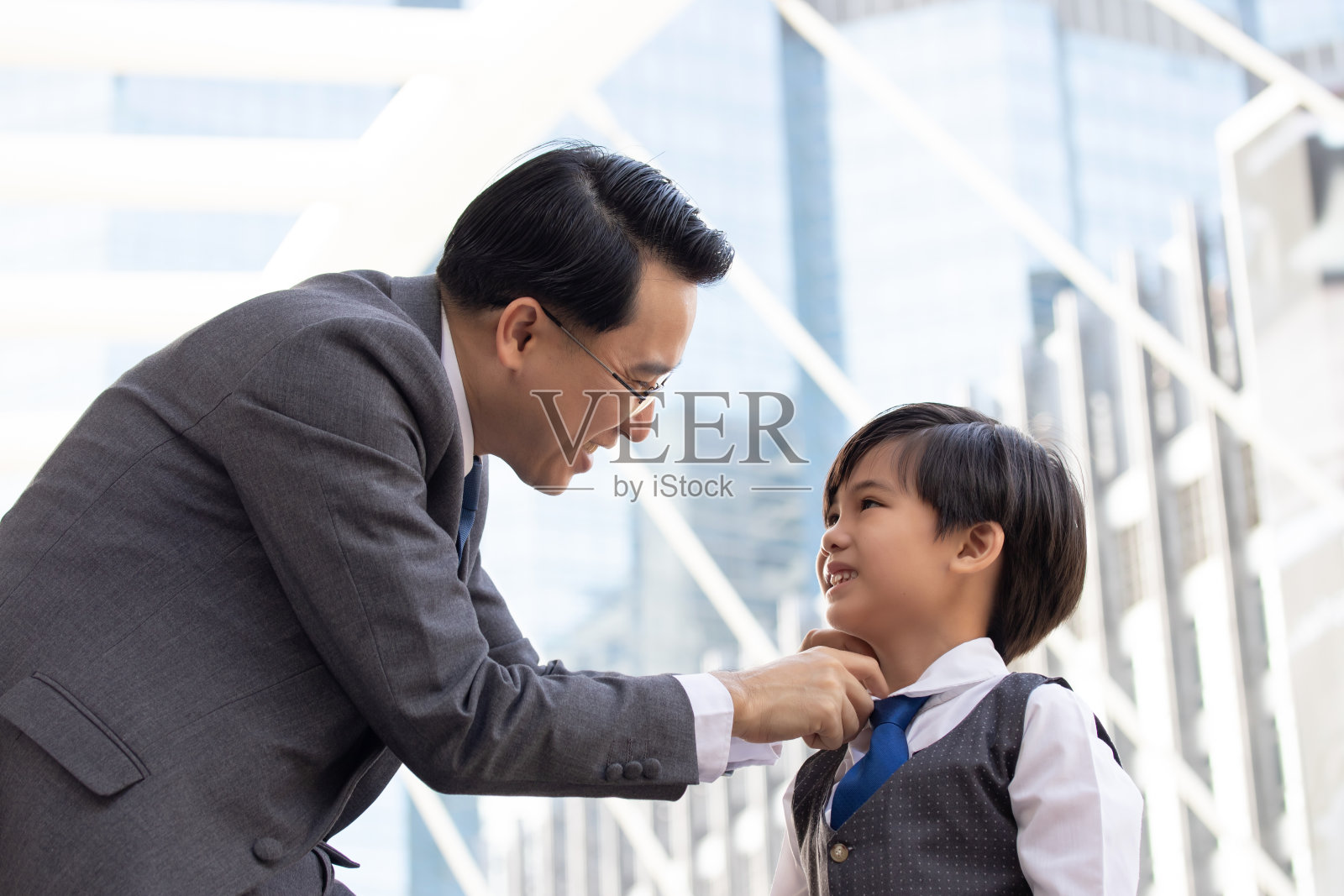 亚洲商业父子自信的孩子想要像他的父亲父母和年轻的男孩一样站在城市与城市景观的背景下规划未来的生活。父亲为儿子检查衣服的经营理念。照片摄影图片