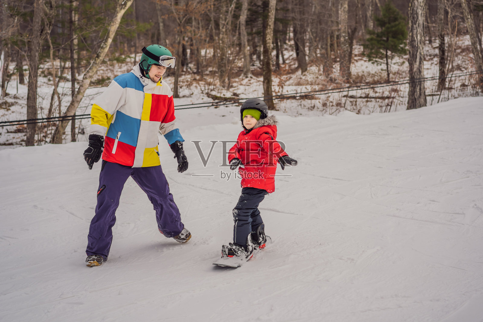 单板教练教一个男孩单板滑雪。冬季儿童活动。孩子们的冬季运动。生活方式照片摄影图片