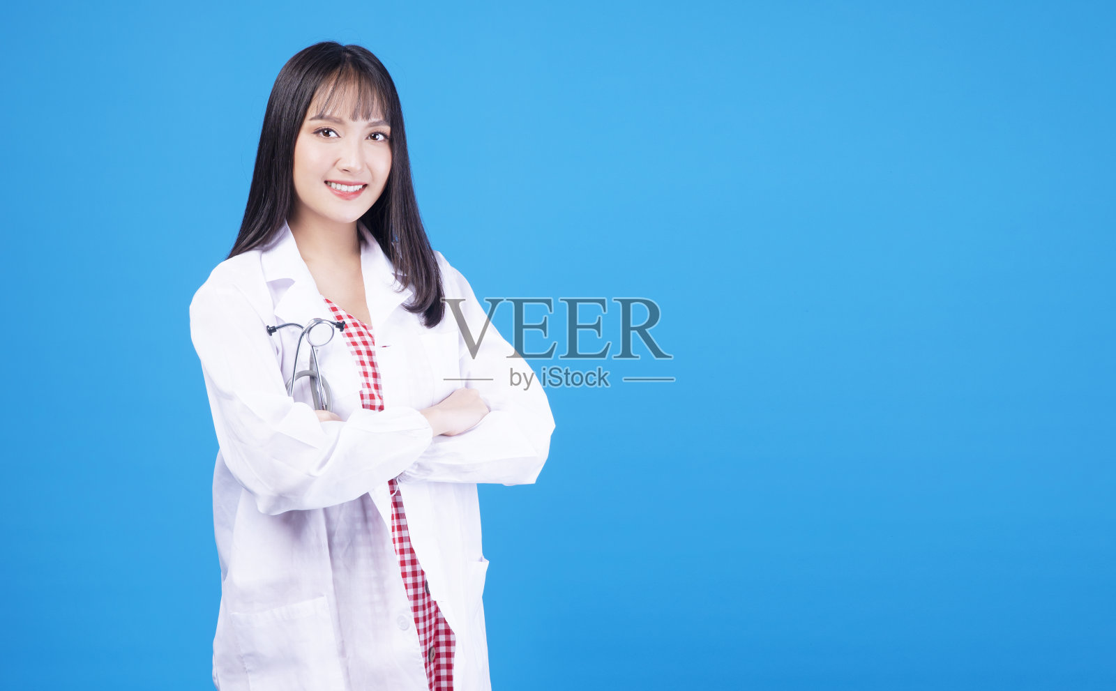 保健职业概念。积极，骄傲，微笑，友好的医生或护士，年轻的女士，穿着统一的外套，双臂交叉，听诊器，站在独立的蓝色背景上。照片摄影图片