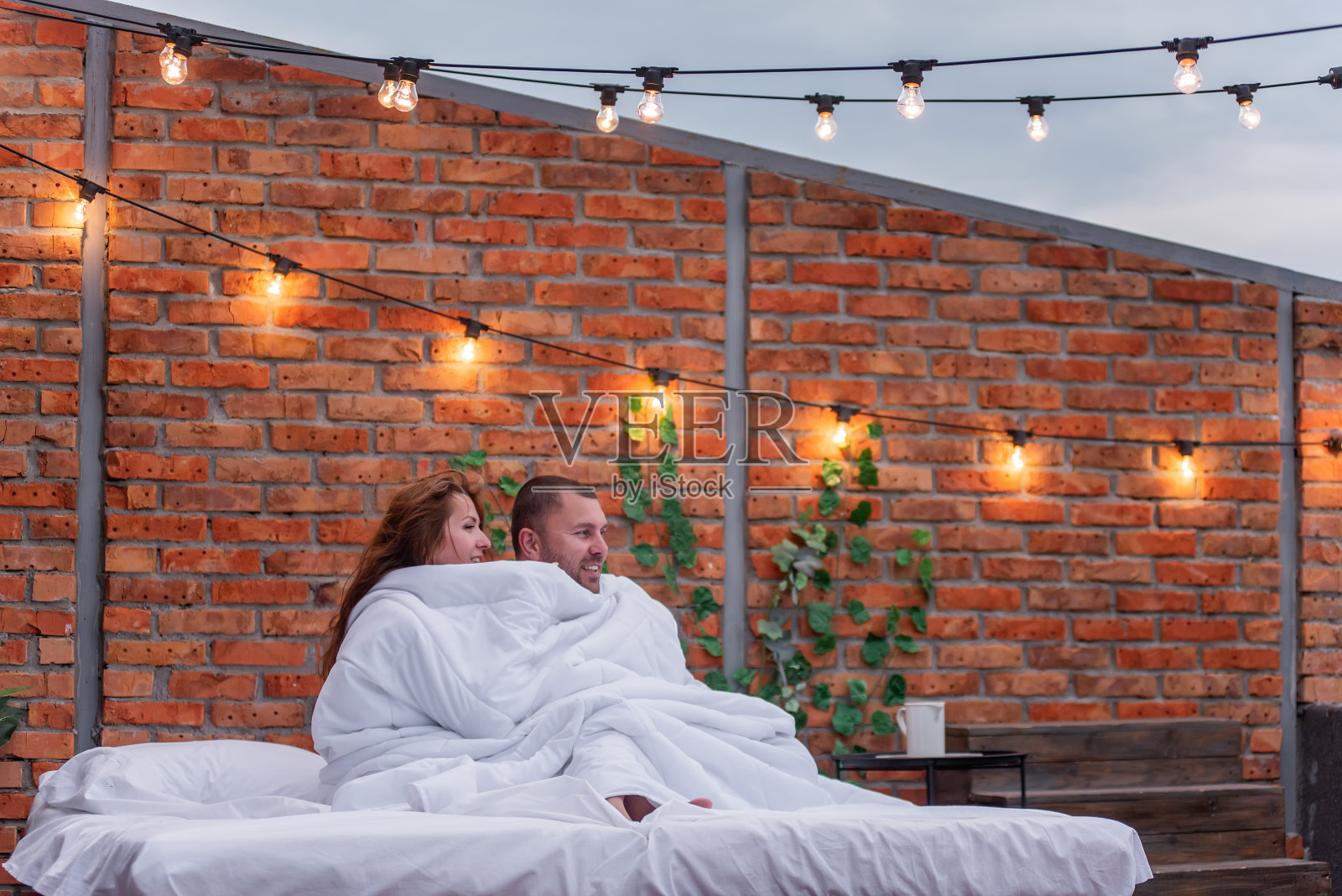 清晨，千禧一代的情侣们裹着白色毯子拥抱在一起，看着城市的风景照片摄影图片