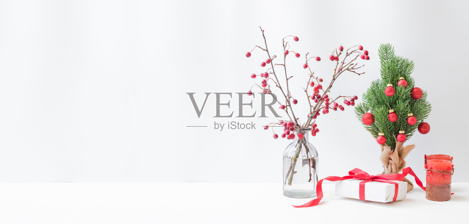 圣诞节、新年家居装饰。玻璃花瓶里有红色浆果的树枝，圣诞树，浅色背景上的礼品盒。用来展示作品的模型照片摄影图片