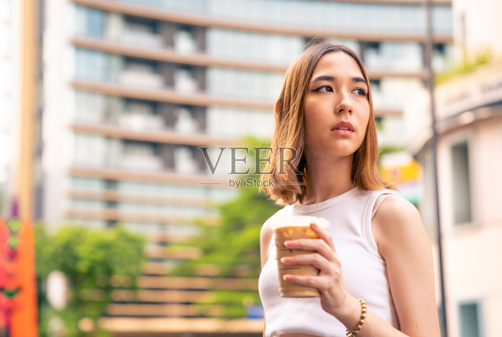 年轻的亚洲妇女肖像坐在户外长凳上喝冰咖啡在城市。照片摄影图片