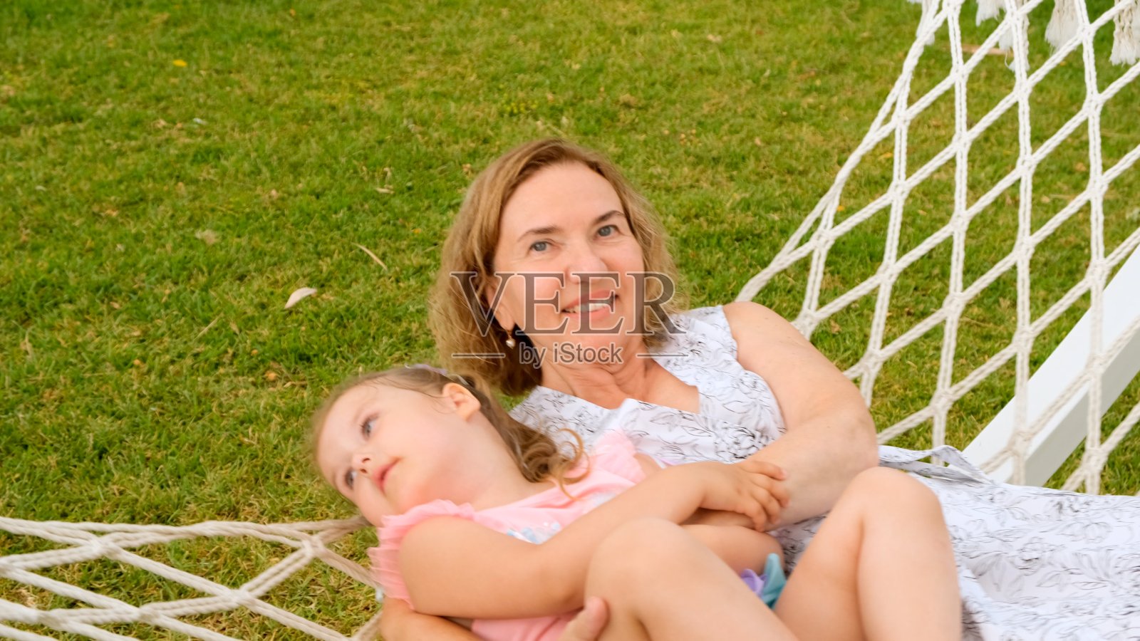 有趣的一对夫妇奶奶和3岁的孙女在一个阳光灿烂的夏天，在他们花园的绿色草地上的吊床上放松和晒太阳。假期观念，世代关系，养育子女，快乐童年照片摄影图片
