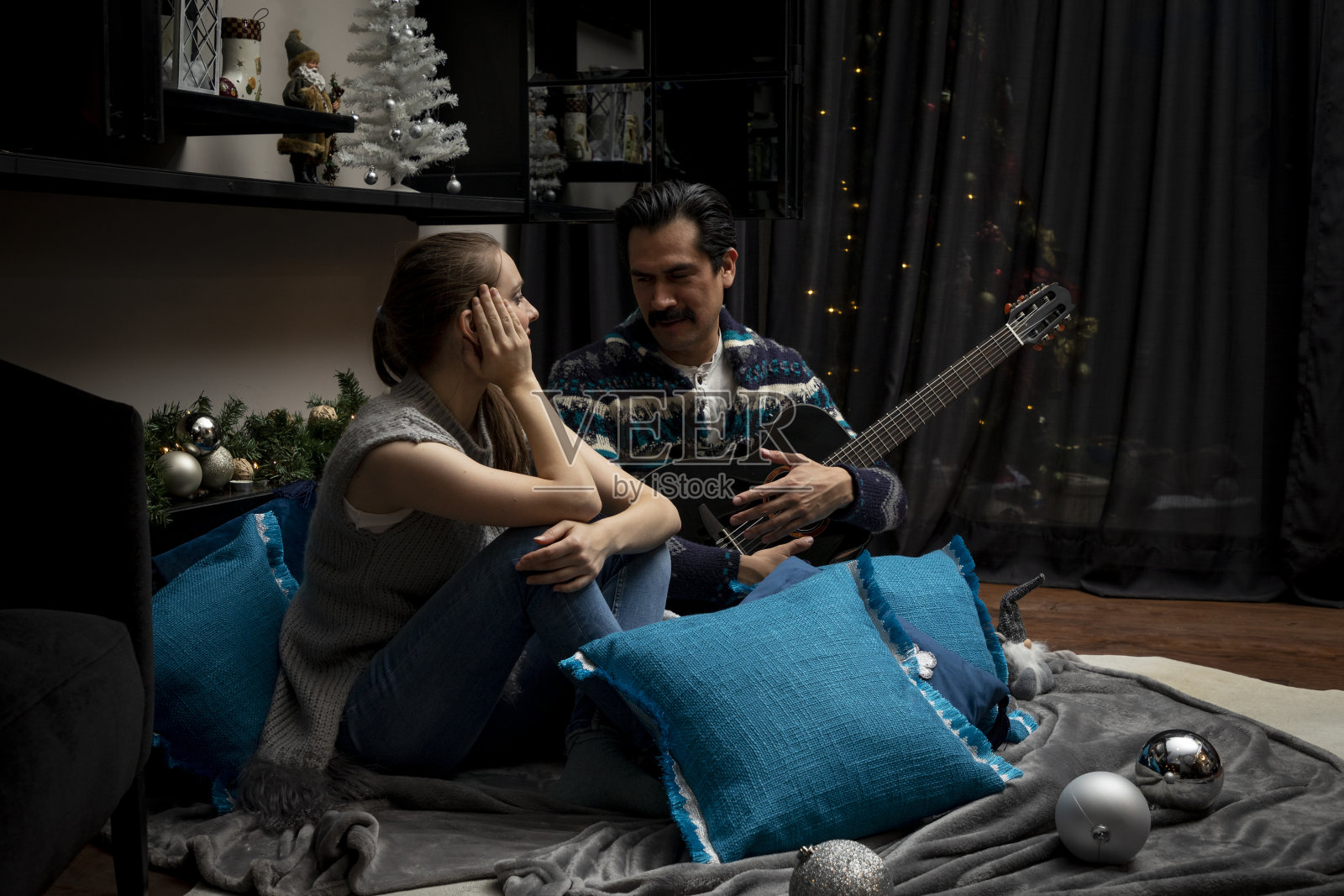 一个圣诞节的晚上，一个男人坐在家里的客厅里，拿着吉他对一个女人唱歌，然后征服了她照片摄影图片