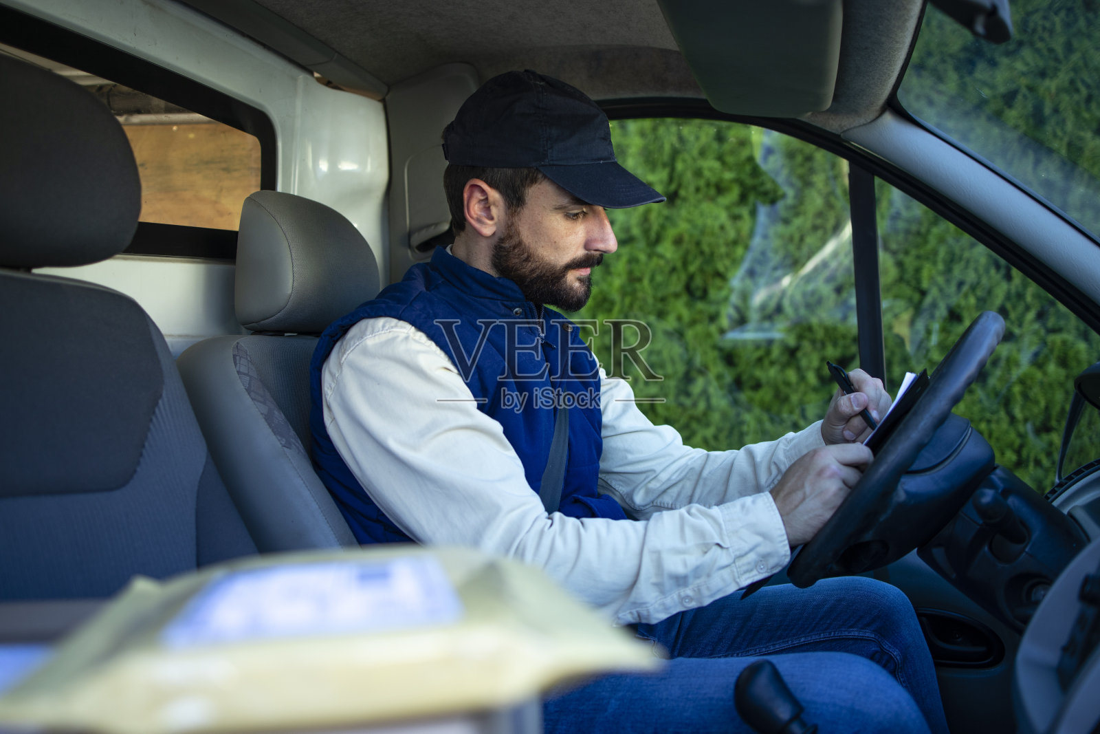 近距离观察包裹运输和送货员司机填写文件在他的货车。照片摄影图片