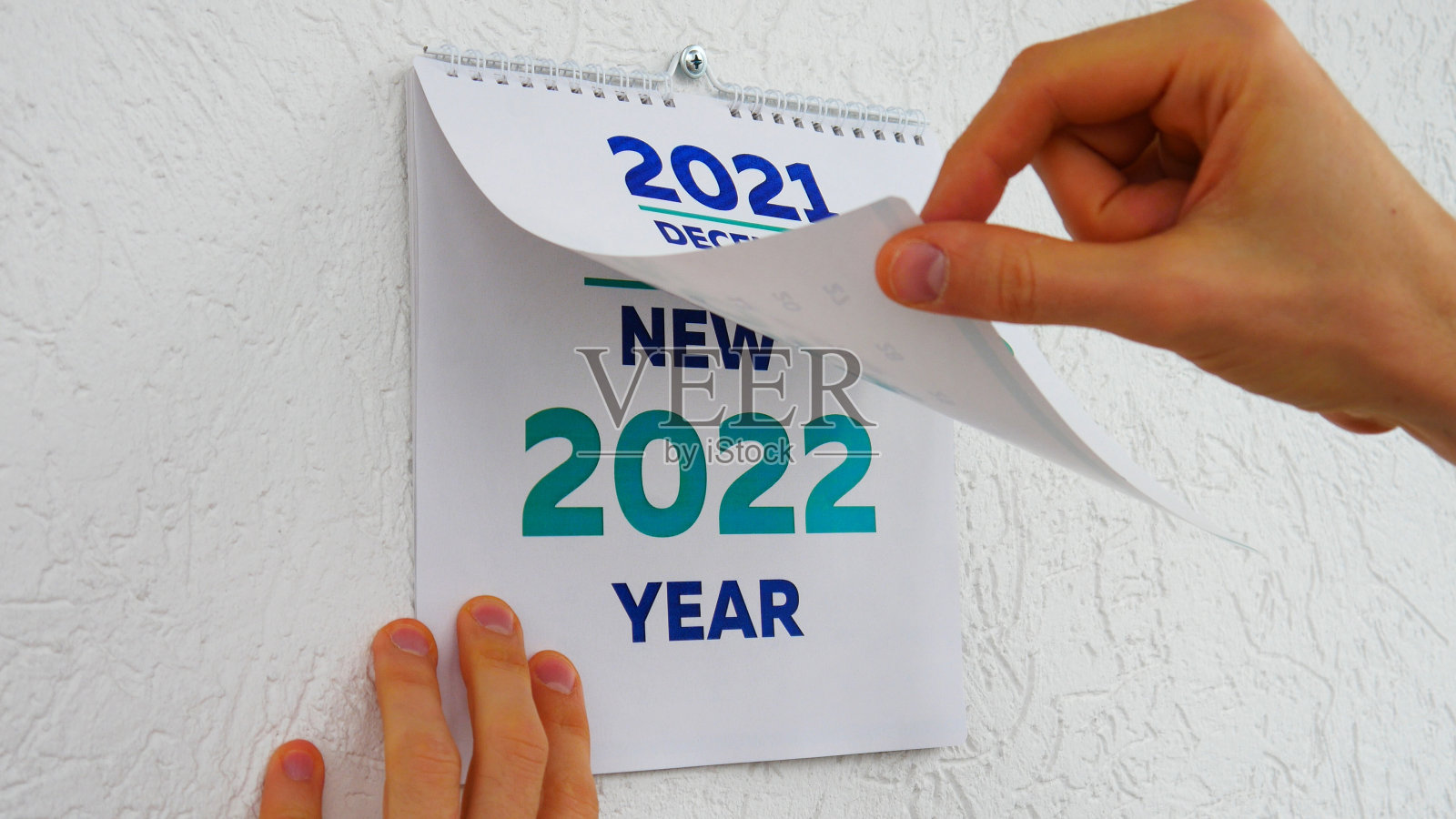 在2021年挂历12月页和2022年新挂历标题页之间，男性的手在翻照片摄影图片