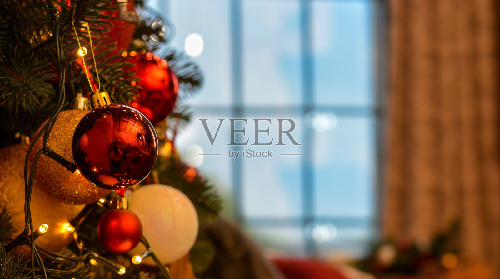 美丽豪华的圣诞树与金色，红色，白色的球，锥形特写的背景上的窗户和棕色窗帘。圣诞气氛!圣诞节的背景照片摄影图片