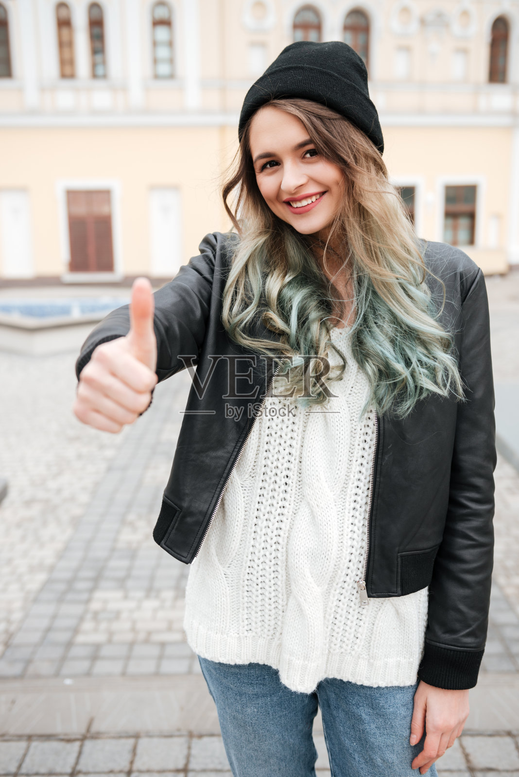 女人走在街上，做出竖起大拇指的手势。照片摄影图片