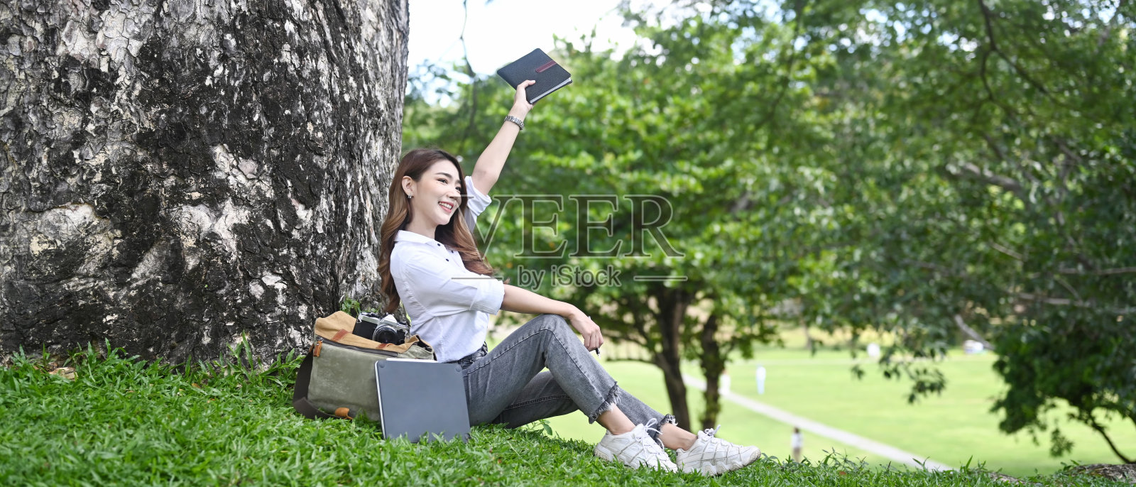 美丽的女人放松和呼吸新鲜的空气，坐在绿草如茵的树下。照片摄影图片