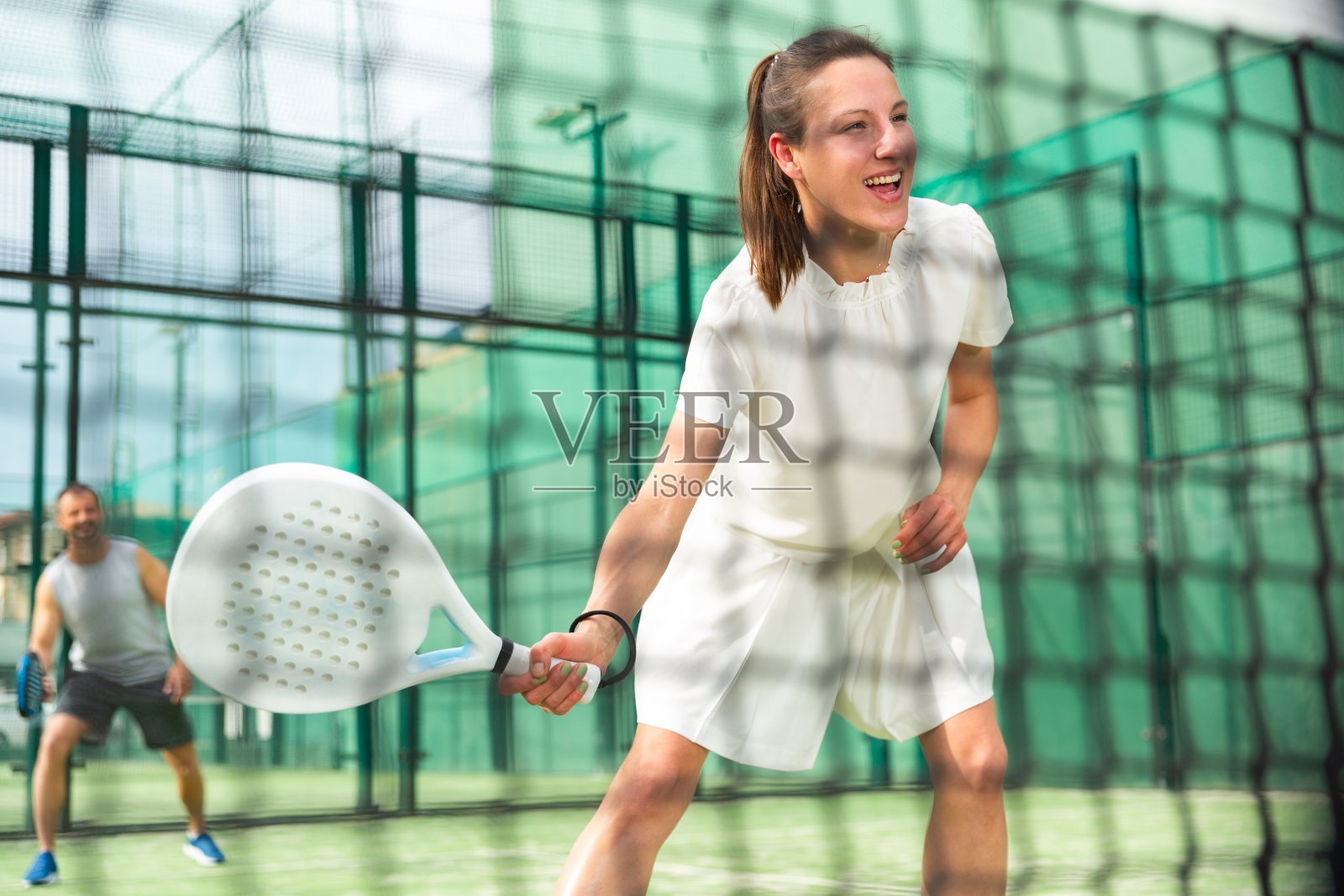 和伙伴一起玩飞盘的运动女人。透过网球网观看照片摄影图片