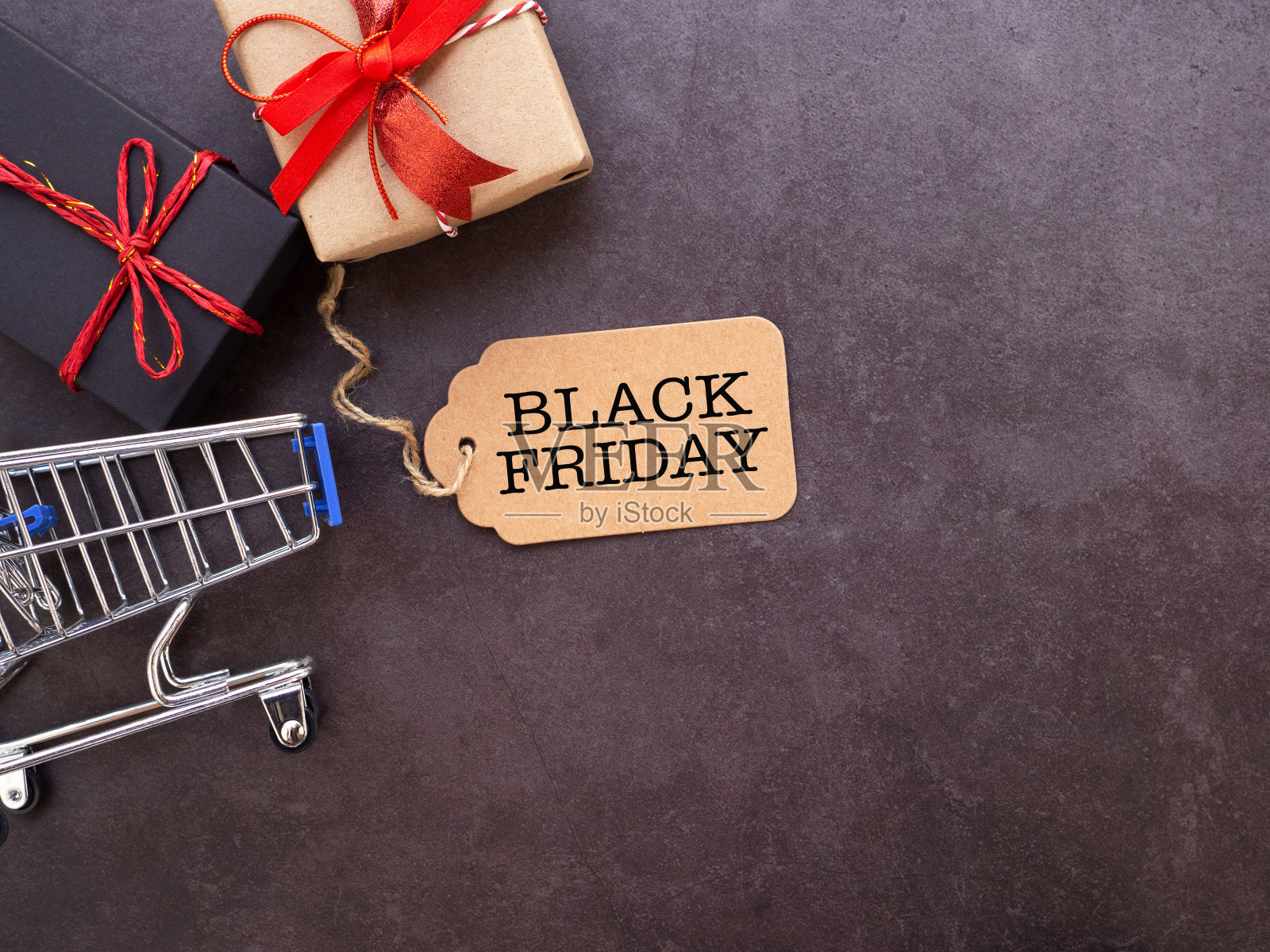 顶视图，棕色标签文本“黑色星期五”和购物车，礼品盒在深灰色背景。平铺，复制空间。照片摄影图片