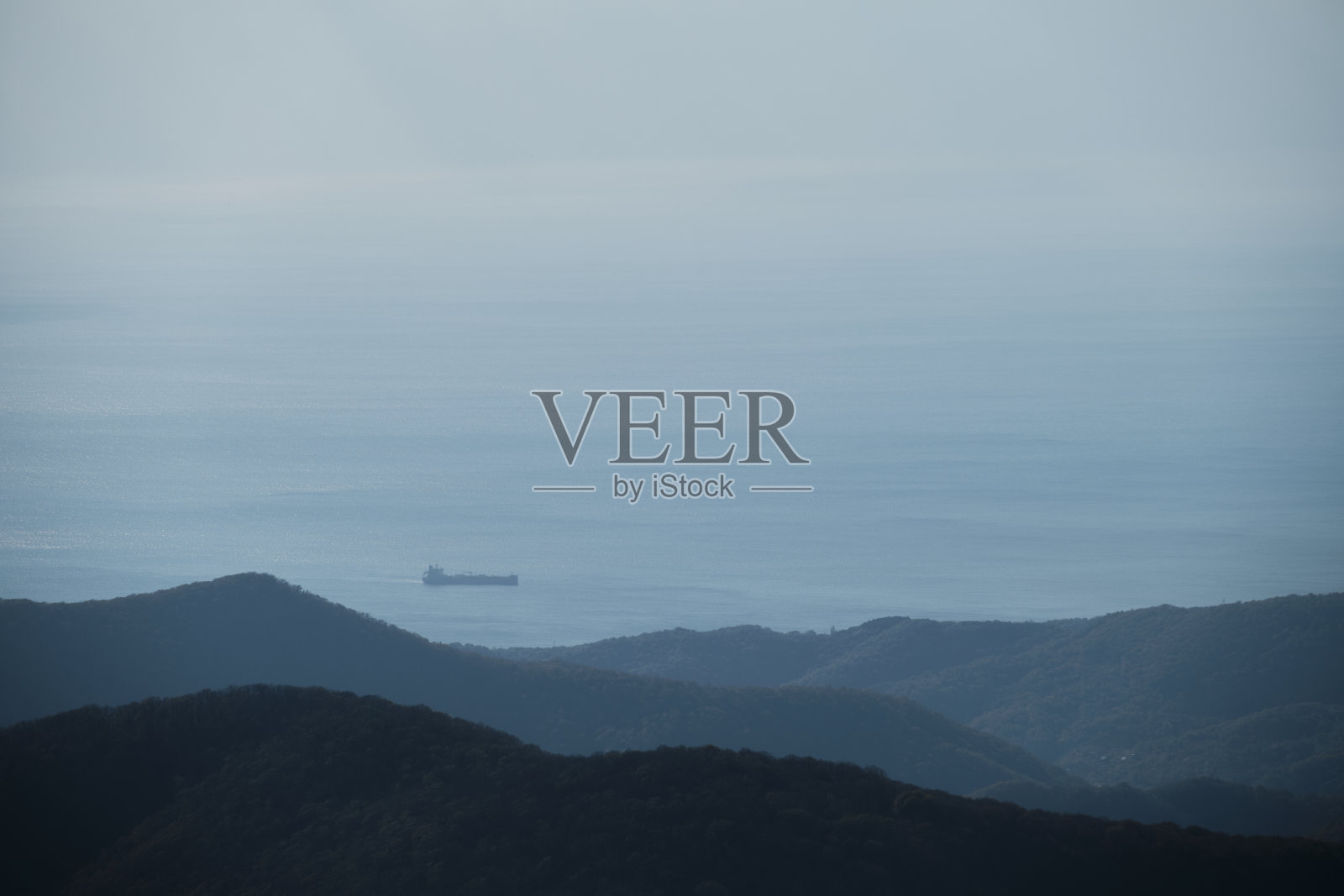 地平线上是大海，远处是货船的小轮廓。晴朗温暖的天气和阴霾笼罩着海面。从山顶和森林的美丽景色。照片摄影图片