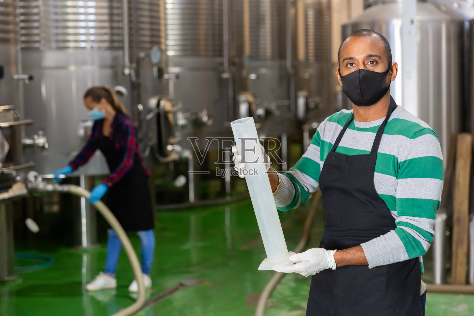 带着面具的酿酒师在工厂检查葡萄酒照片摄影图片
