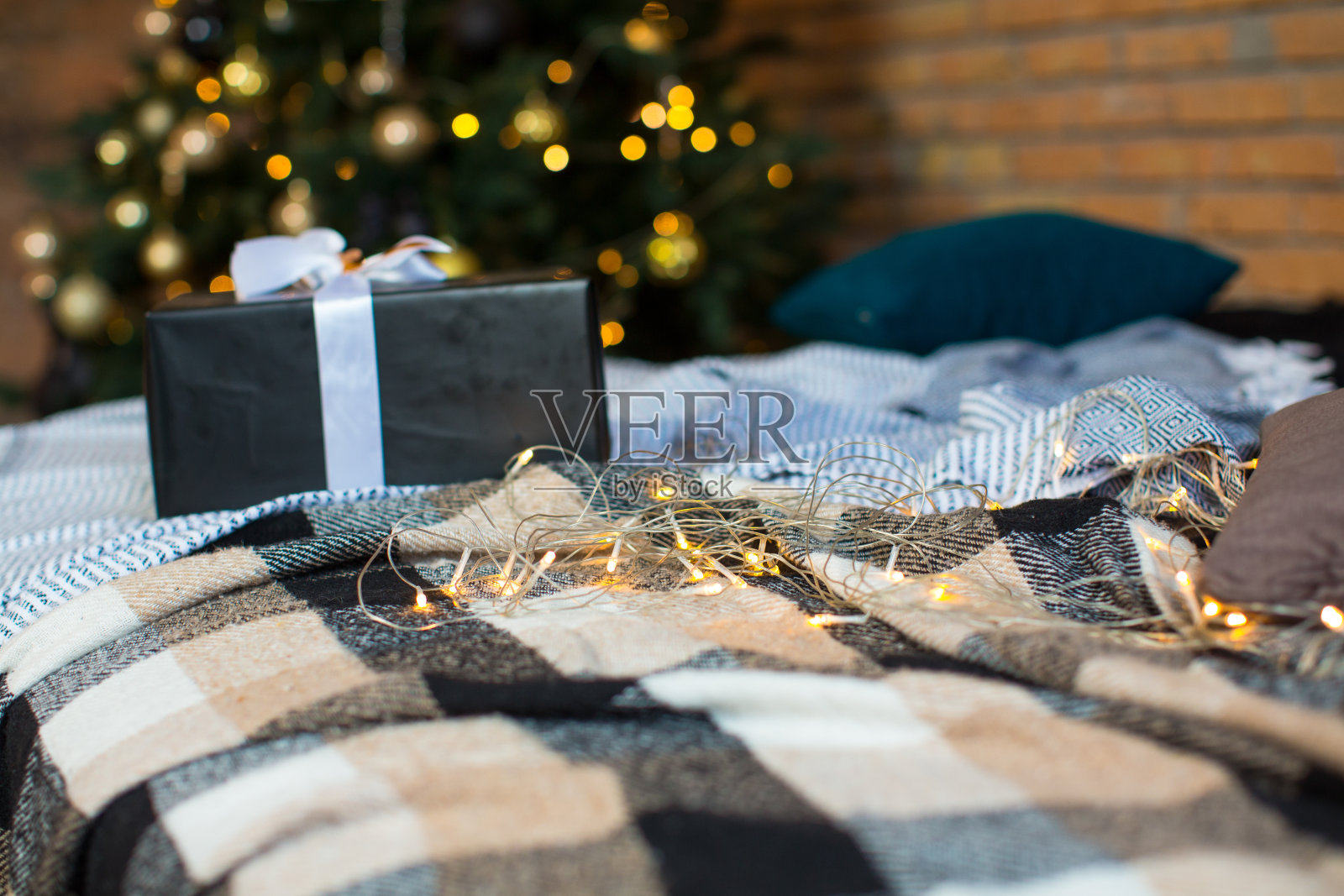 床上放着一个带银色蝴蝶结的黑色盒子，背景是圣诞树和闪闪发光的花环灯照片摄影图片