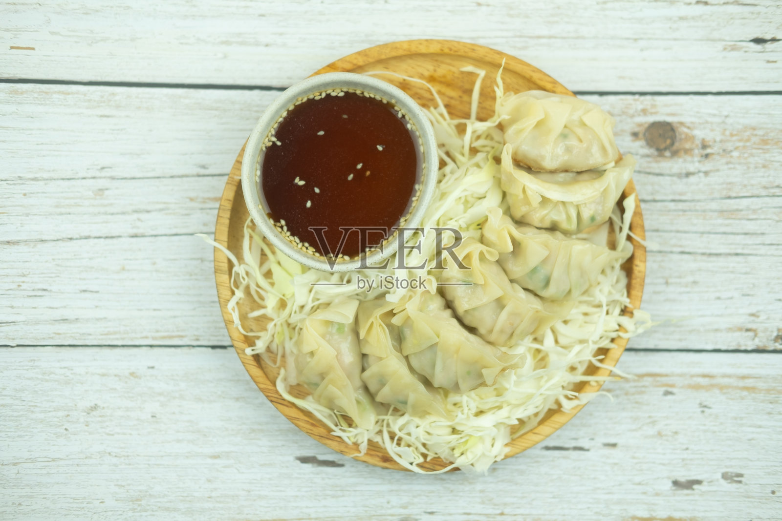 木盘上的蒸饺配上切碎的卷心菜，木桌上放着酱油照片摄影图片