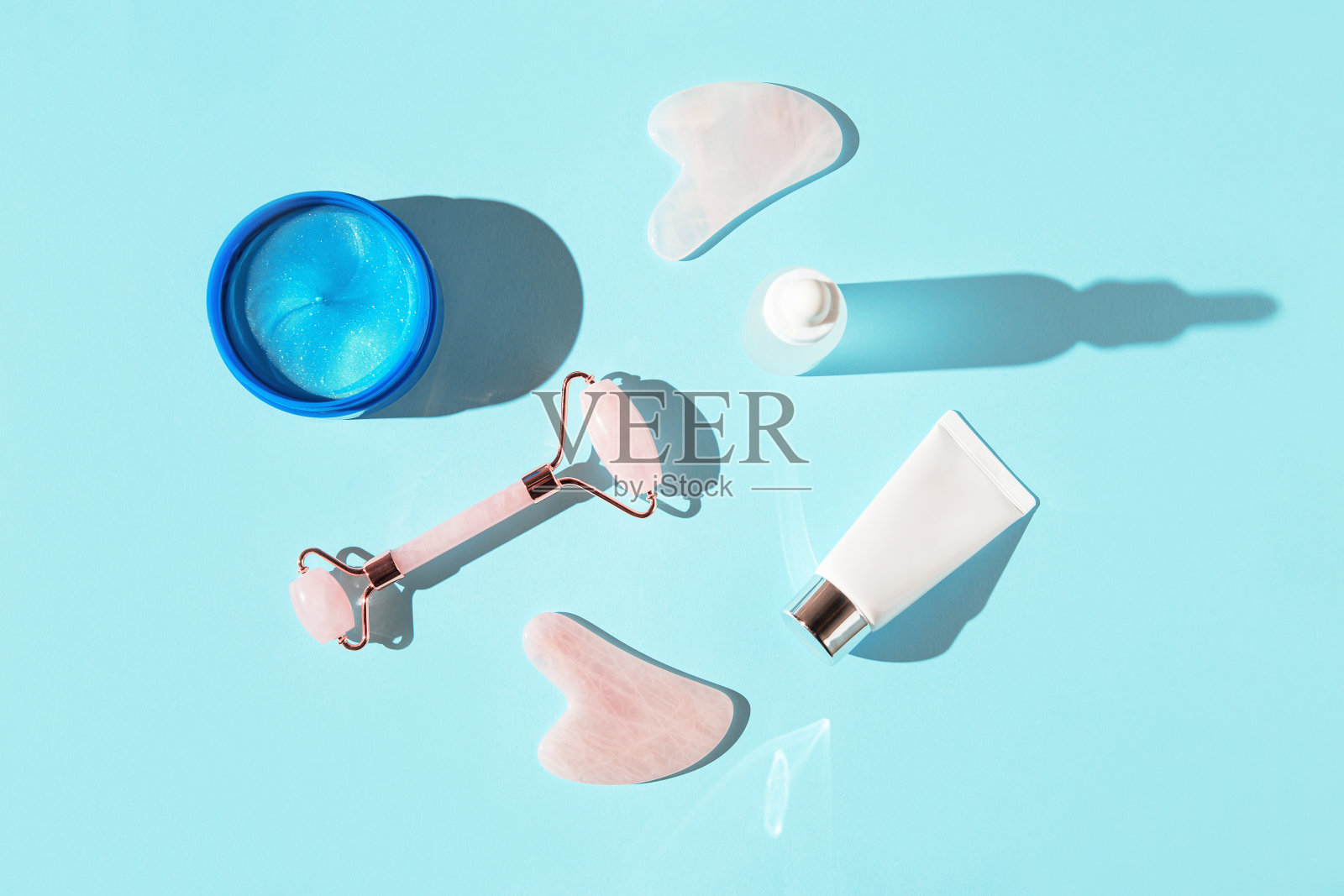 家用皮肤护理和水疗美容包。胶原蛋白眼罩，面膜和刮痧按摩器，一瓶精油或血清在蓝色柔和的阳光下。前视图。平躺照片摄影图片