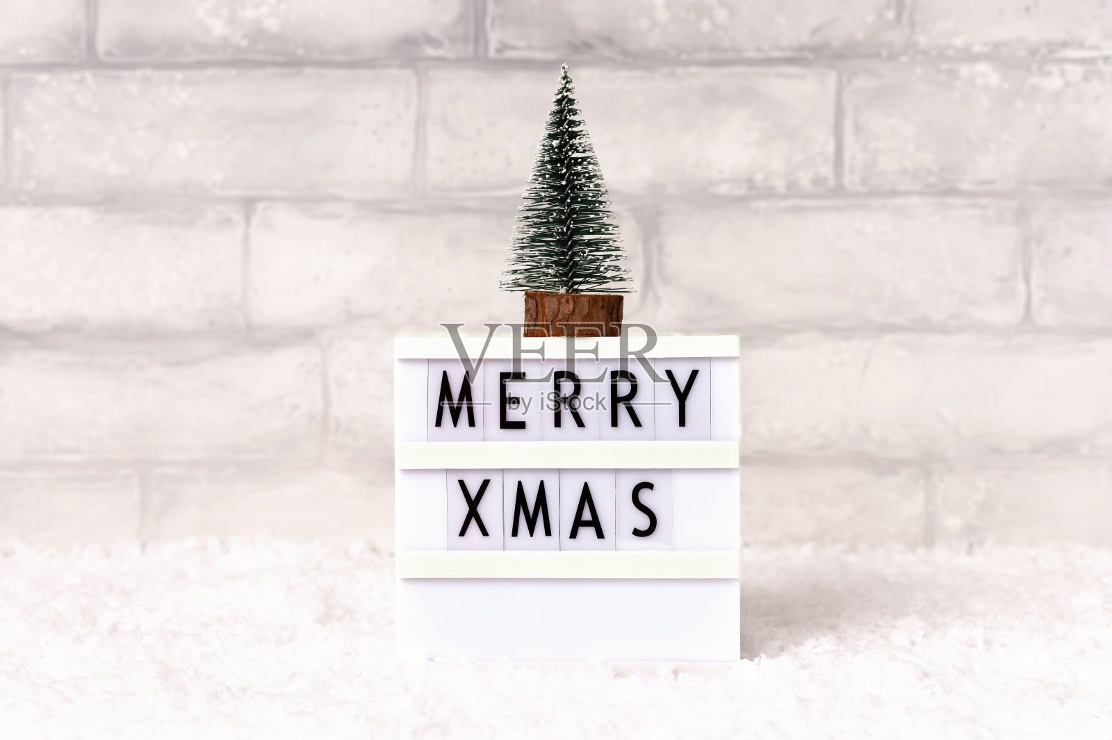 微型冷杉树，圣诞节时带有merry xmas字样的灯箱，背景有雪，正面视图照片摄影图片