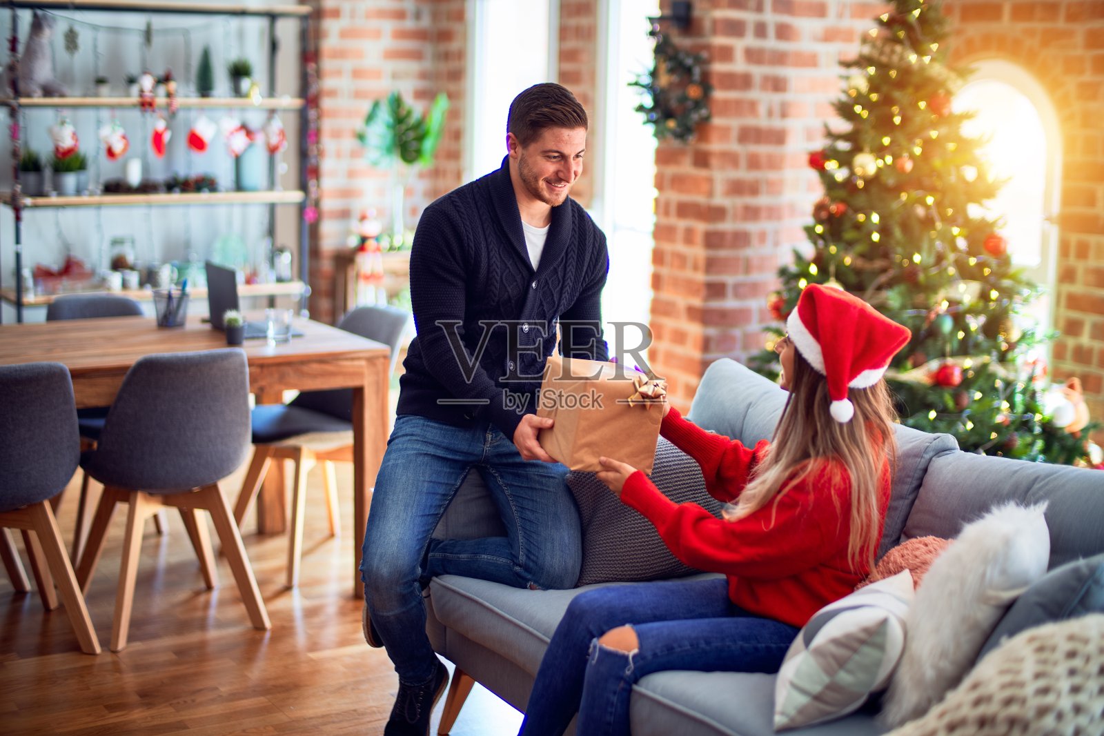 年轻漂亮的夫妇微笑着，幸福而自信。男人在家里的圣诞树旁给女人送礼物照片摄影图片