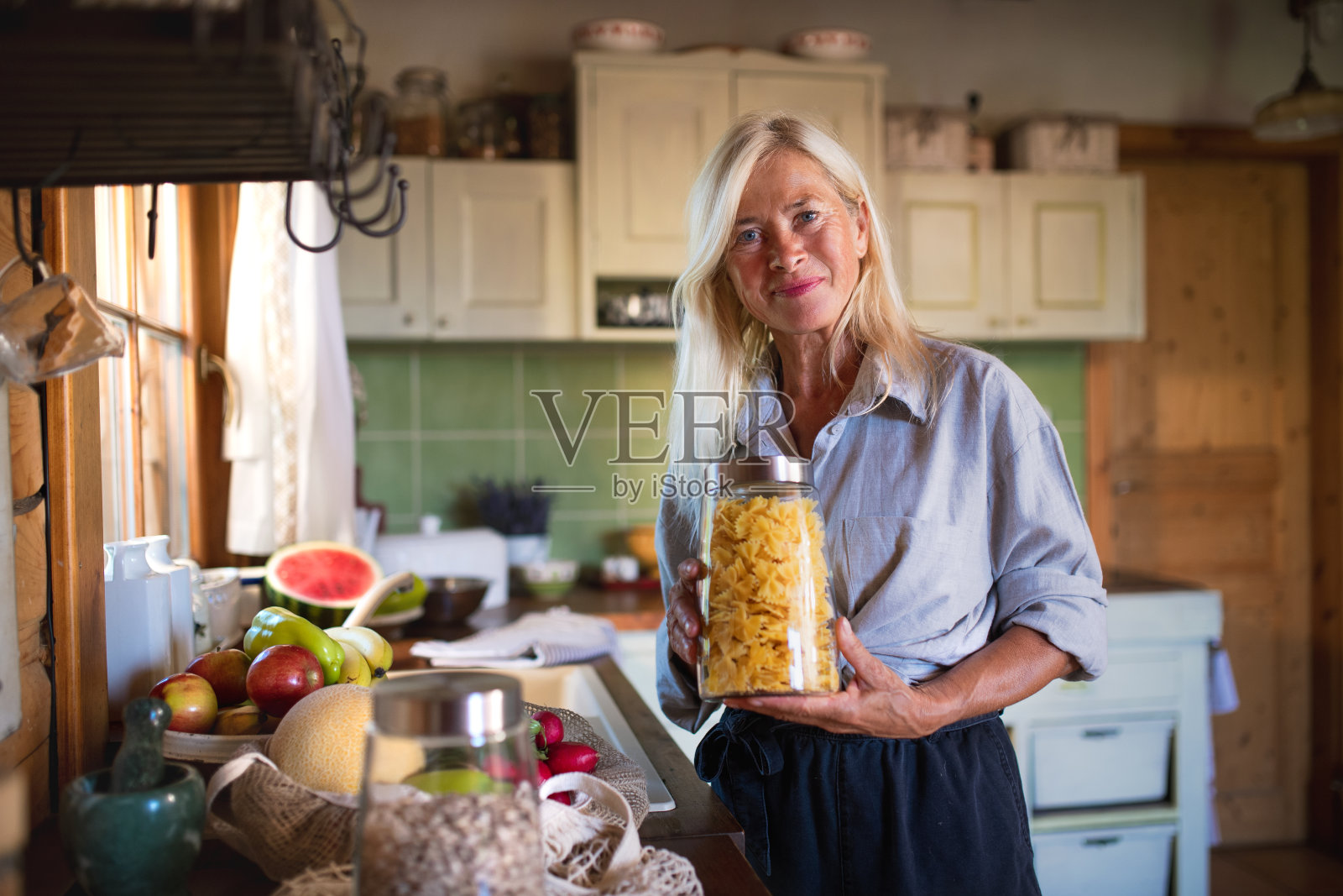 快乐的老年妇女打开行李，在家里购物，看着相机，可持续的生活方式。照片摄影图片