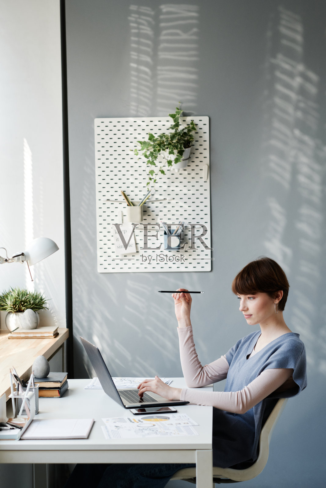 忙碌的有吸引力的女孩拿着铅笔和分析数据的笔记本电脑，而工作在舒适的家庭办公室照片摄影图片