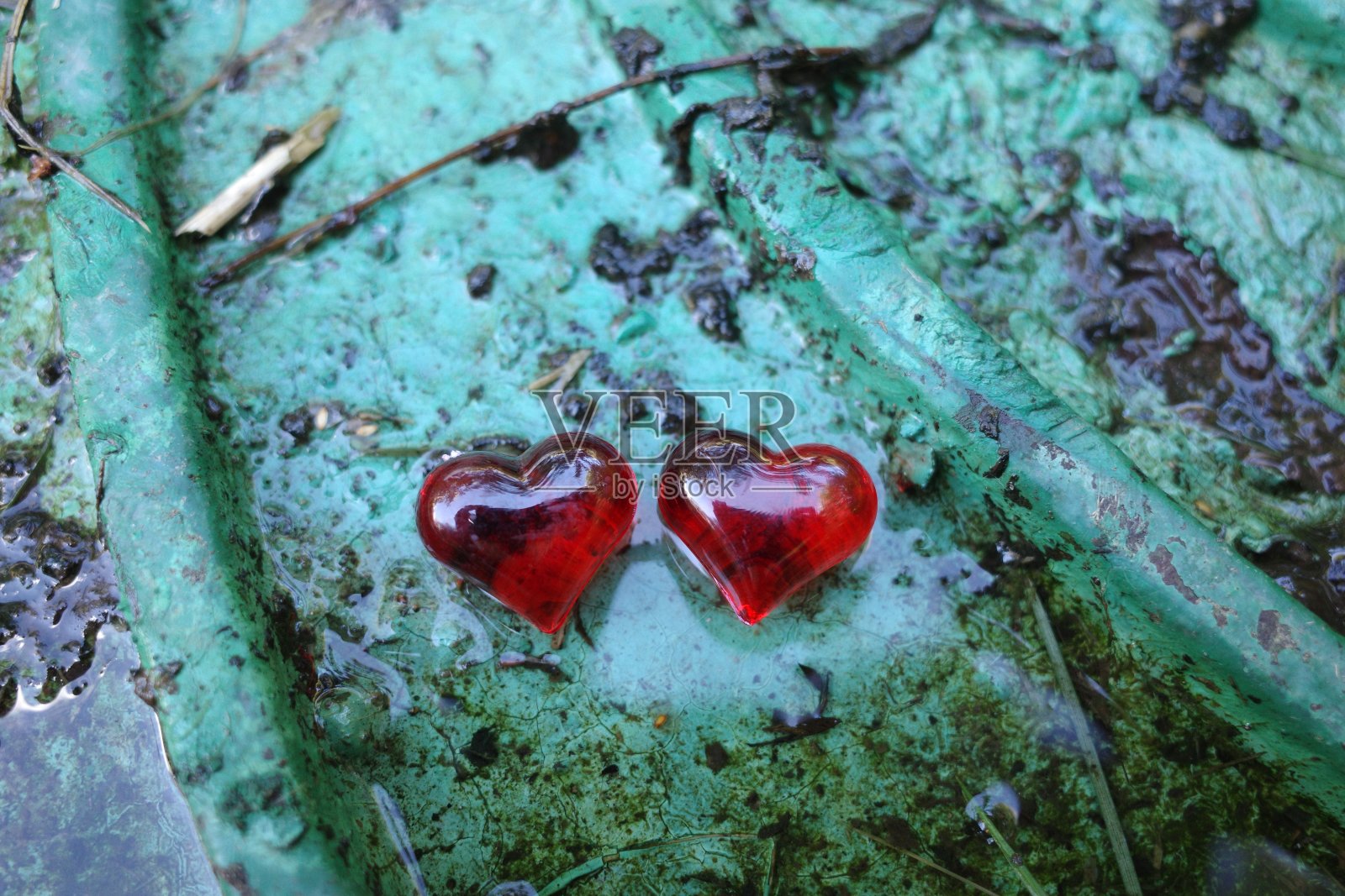 两个红红的心形湿漉漉的，雨后脏兮兮的绿色井盖。浪漫的背景照片摄影图片