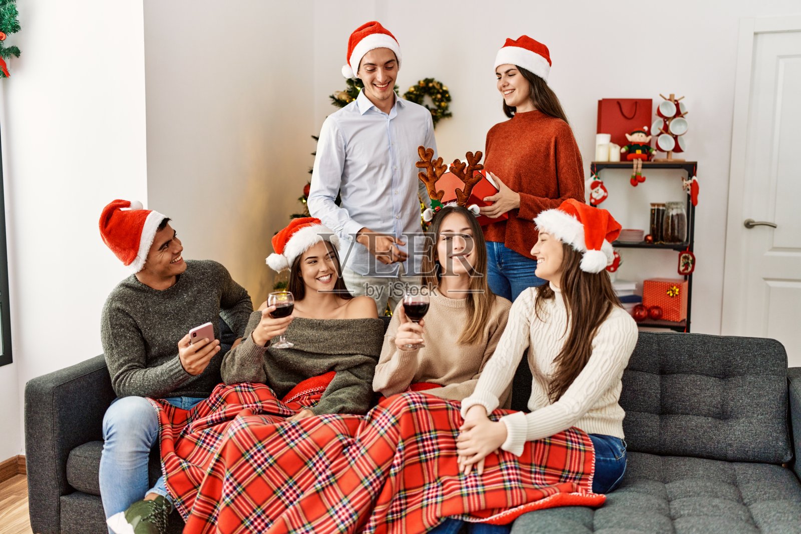 一群年轻人坐在家里的沙发上，一边喝酒一边用手机庆祝圣诞节。照片摄影图片