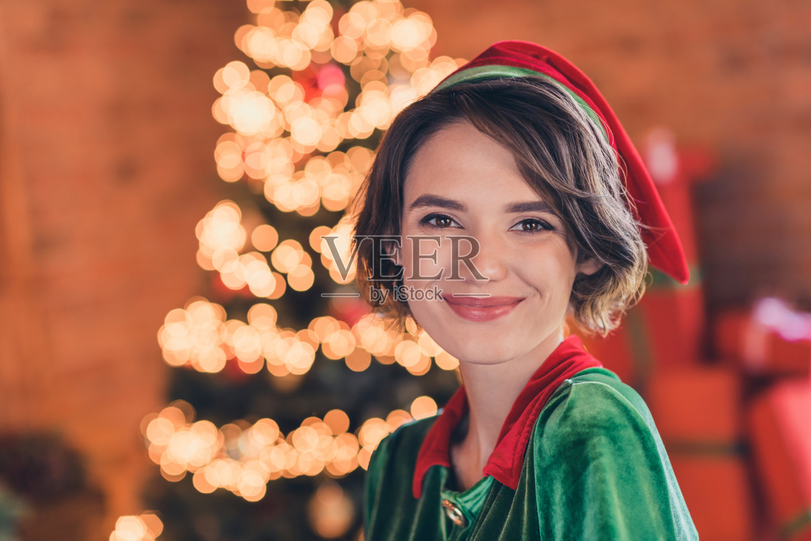 可爱可爱的年轻女士穿着小精灵的衣服庆祝圣诞节，微笑着在室内的家的房间照片摄影图片