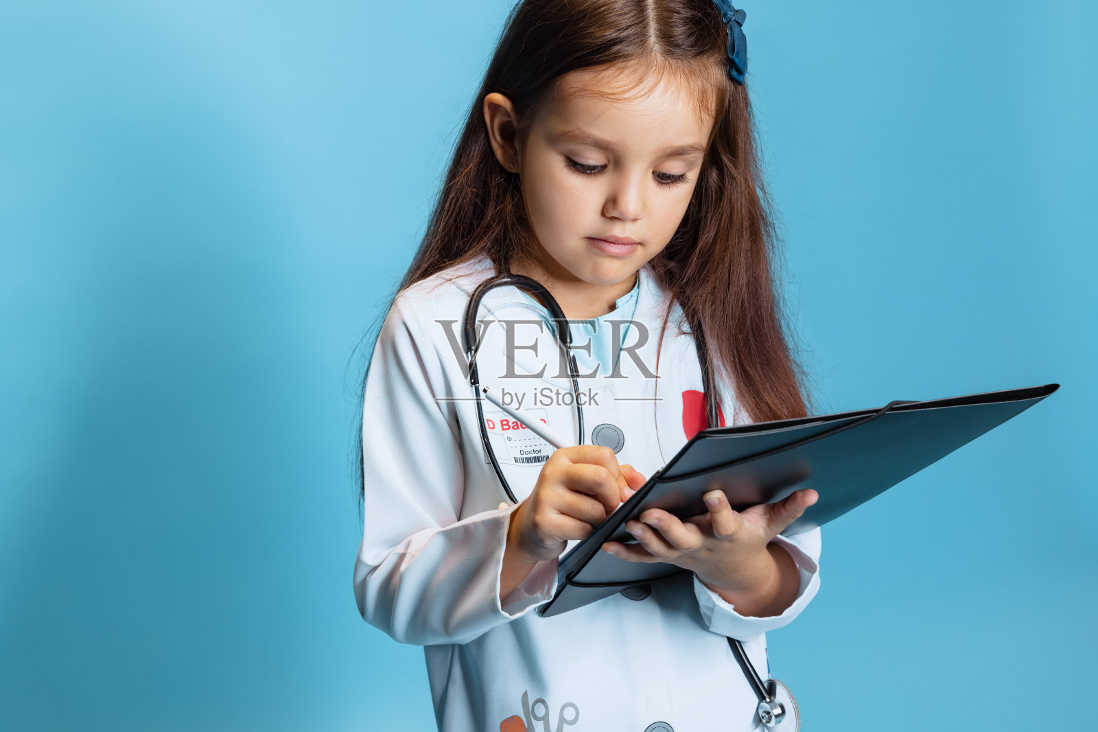 学前班美丽的女孩，医生形象中的孩子穿着白色的药衣，在蓝色工作室背景下孤独地摆姿势照片摄影图片