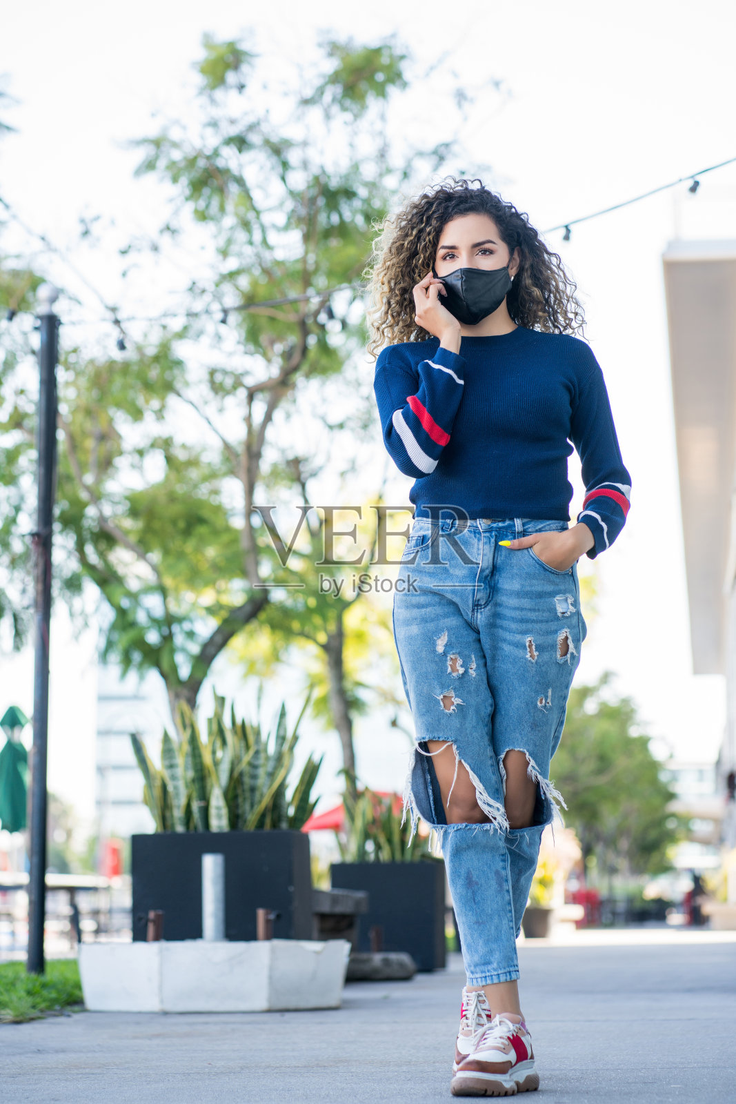 一位拉丁妇女在户外打电话时戴着口罩。照片摄影图片