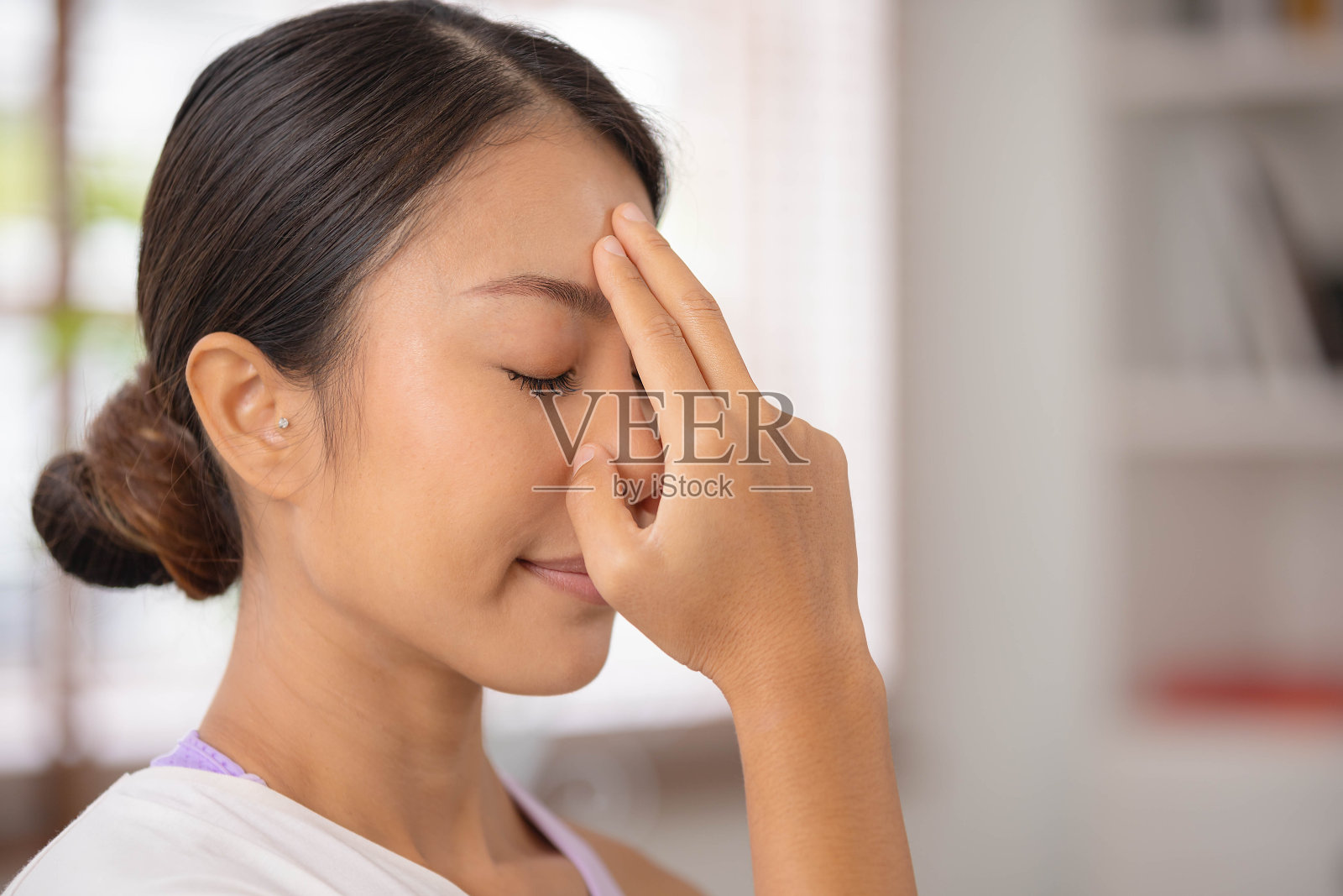 为了引导呼吸，一位亚洲女士用手指触摸自己的前额。从瑜伽和冥想开始照片摄影图片