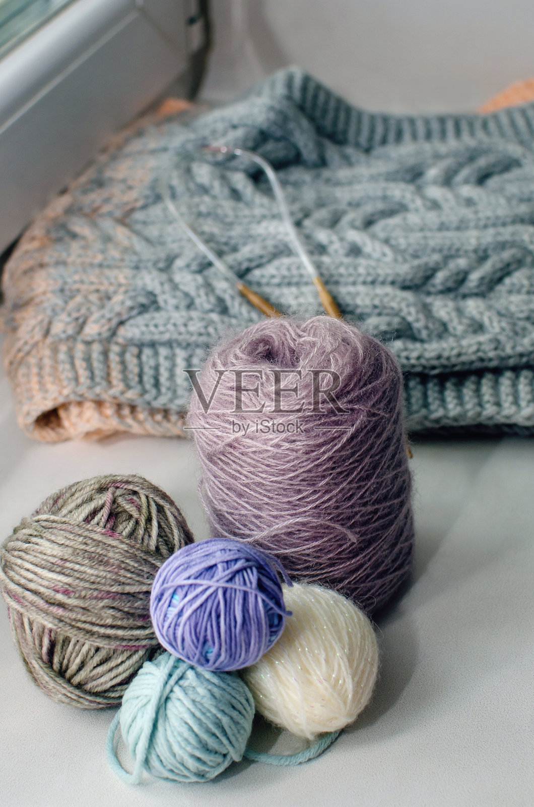 窗台上放着各种颜色的纱线和针织针，旁边是手织毛衣。垂直的摄影。照片摄影图片