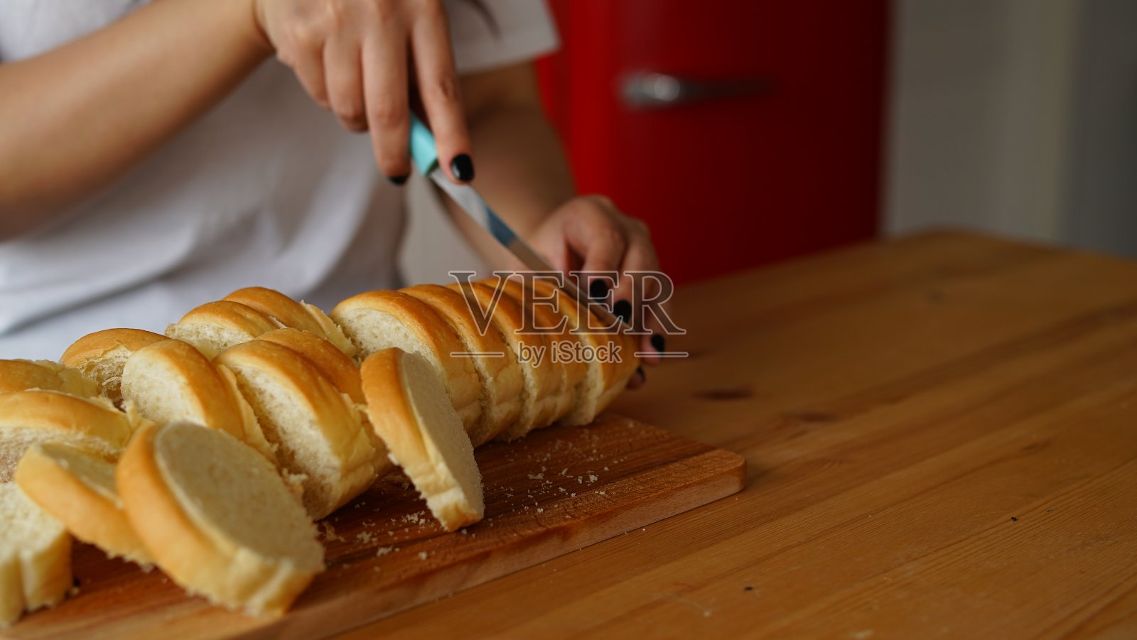 厨房里的女人在木板上切面包的特写镜头。女人的手在厨房桌上的案板上用刀切法棍照片摄影图片