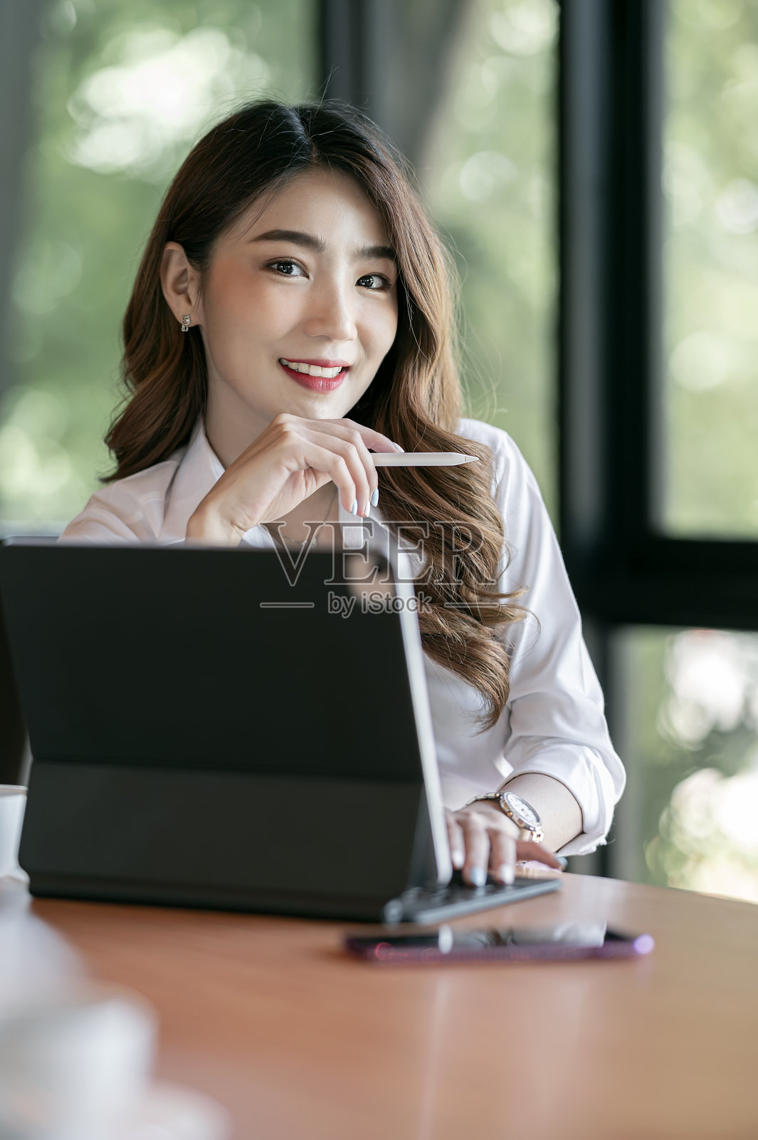 年轻美丽的女商人的肖像微笑和看着相机，而坐在她的办公桌办公室。照片摄影图片