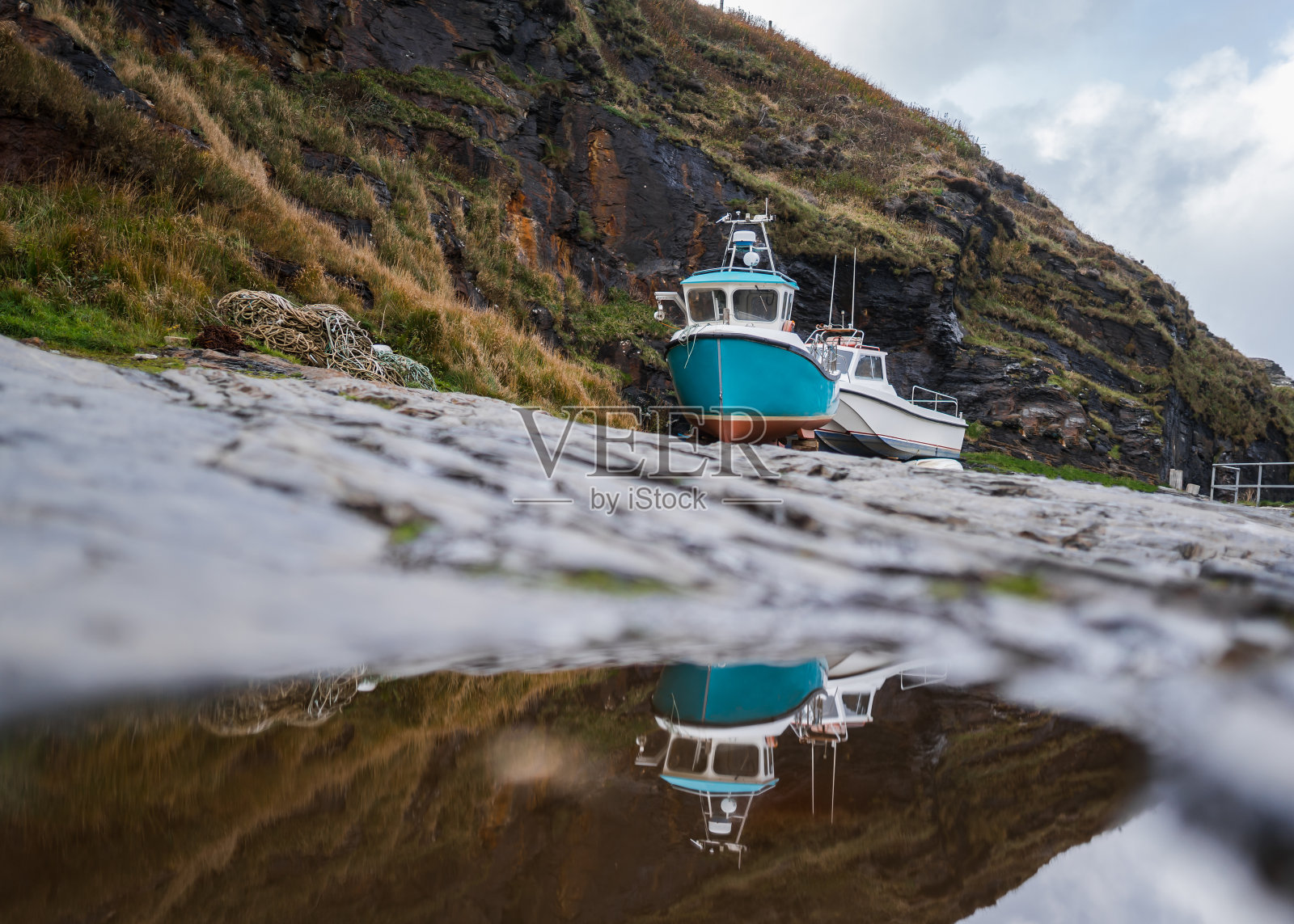旧渔船在干船坞岩壁港系泊修理映在水中照片摄影图片