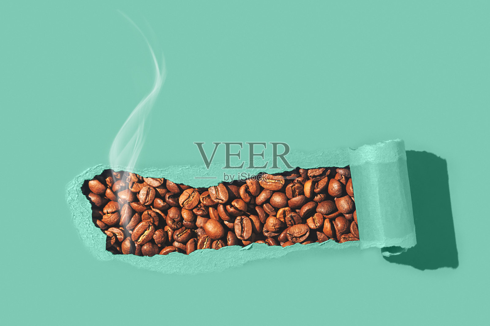 创意咖啡平铺。芳香的咖啡豆穿过撕破的绿纸。照片摄影图片